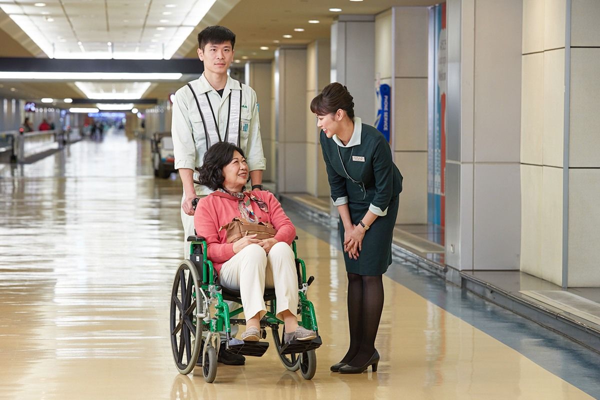 An EVA Air employee pushes a passenger in a wheelchair while a flight attendant talks with the passenger.