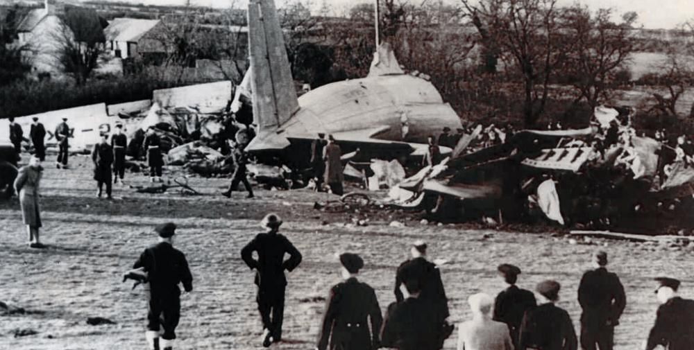 A Black-and-white photo of an aircraft on the ground with only its tail left intact as bystanders approach the scene.