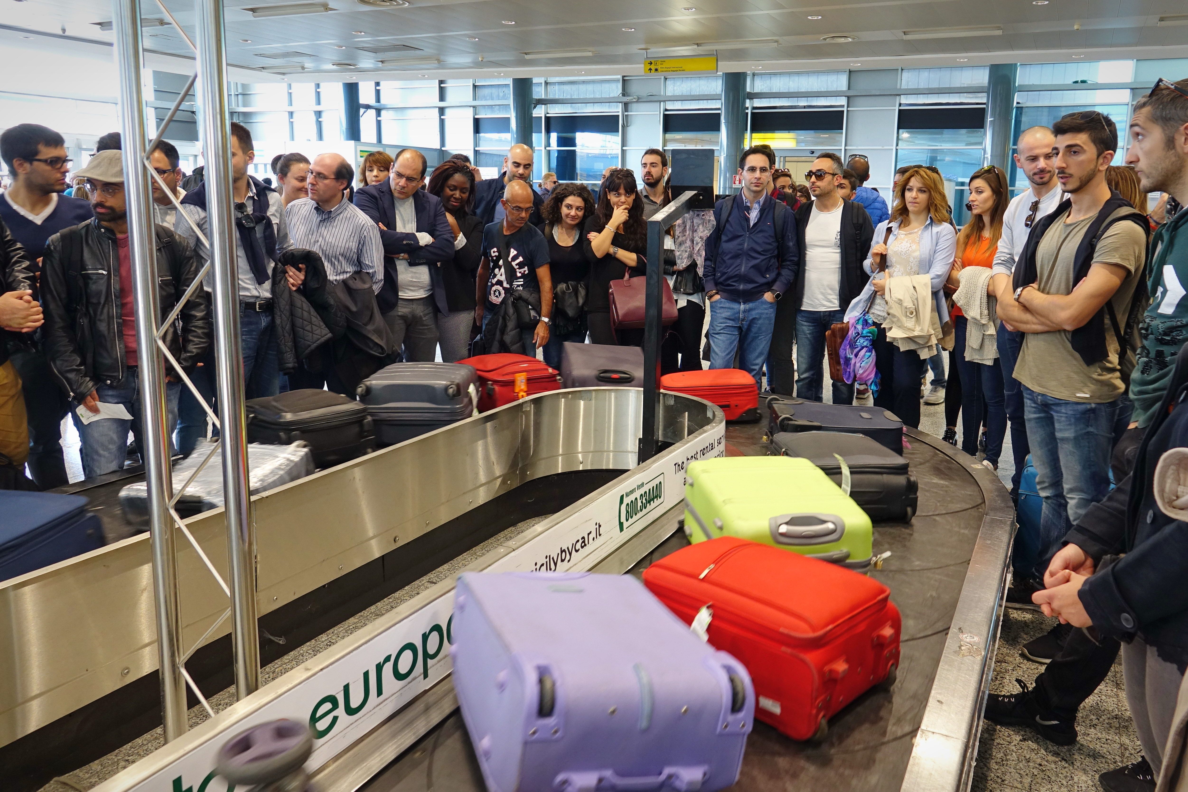 Passengers stand around a luggage carousel with many bags.