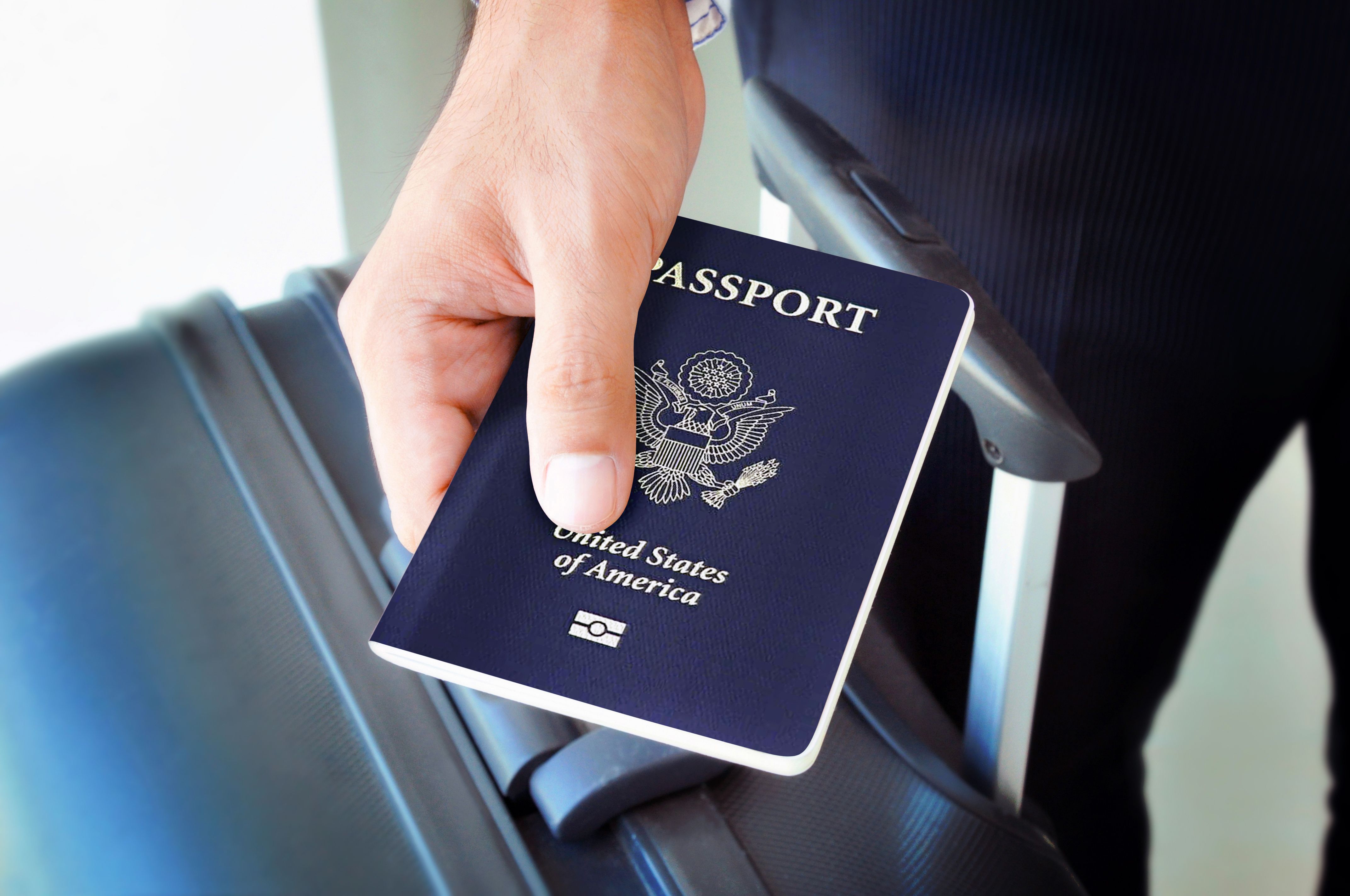 A passenger holds a US Passport while standing next to a suitcase.