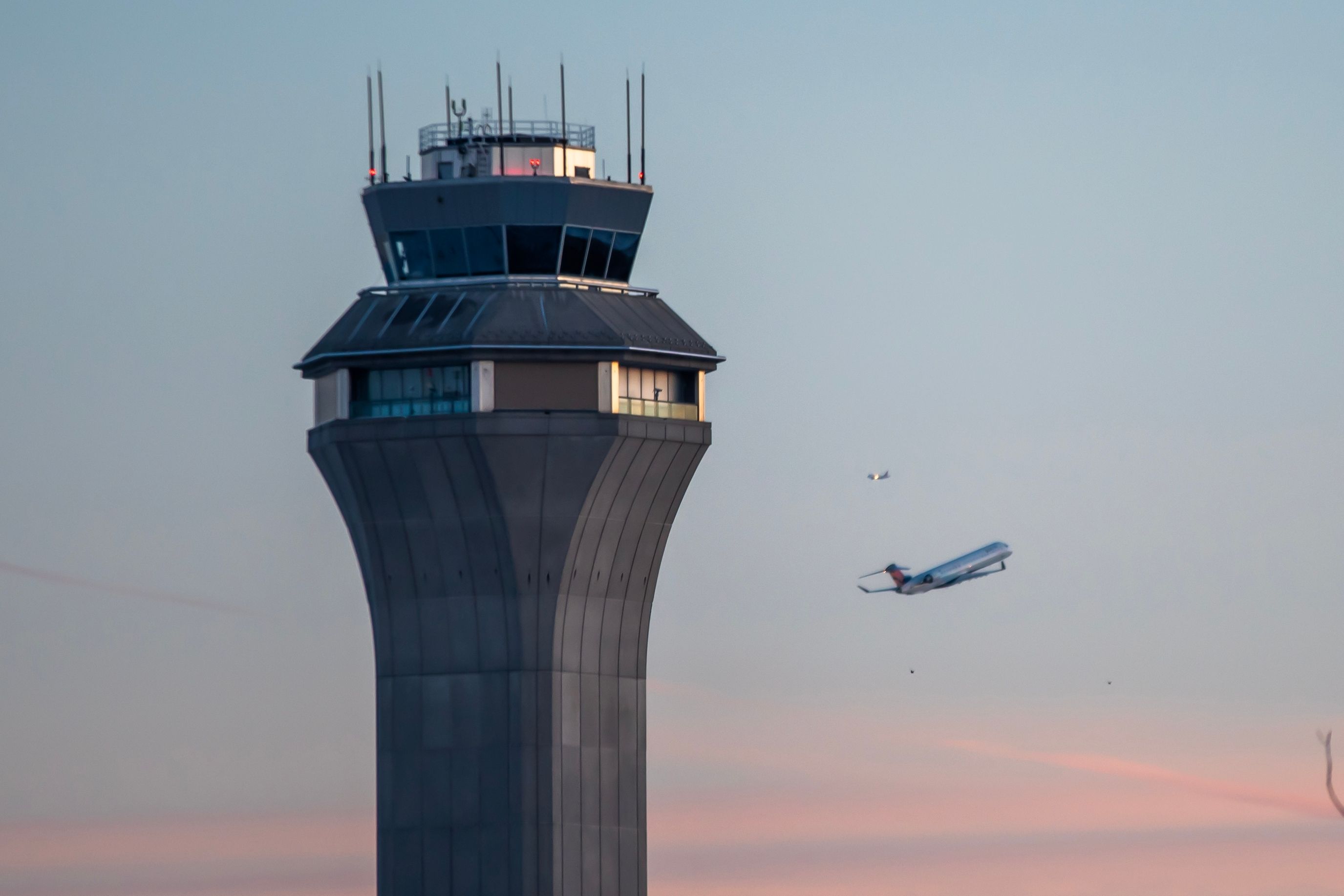 An aircraft flying behind an Air traffic control tower.