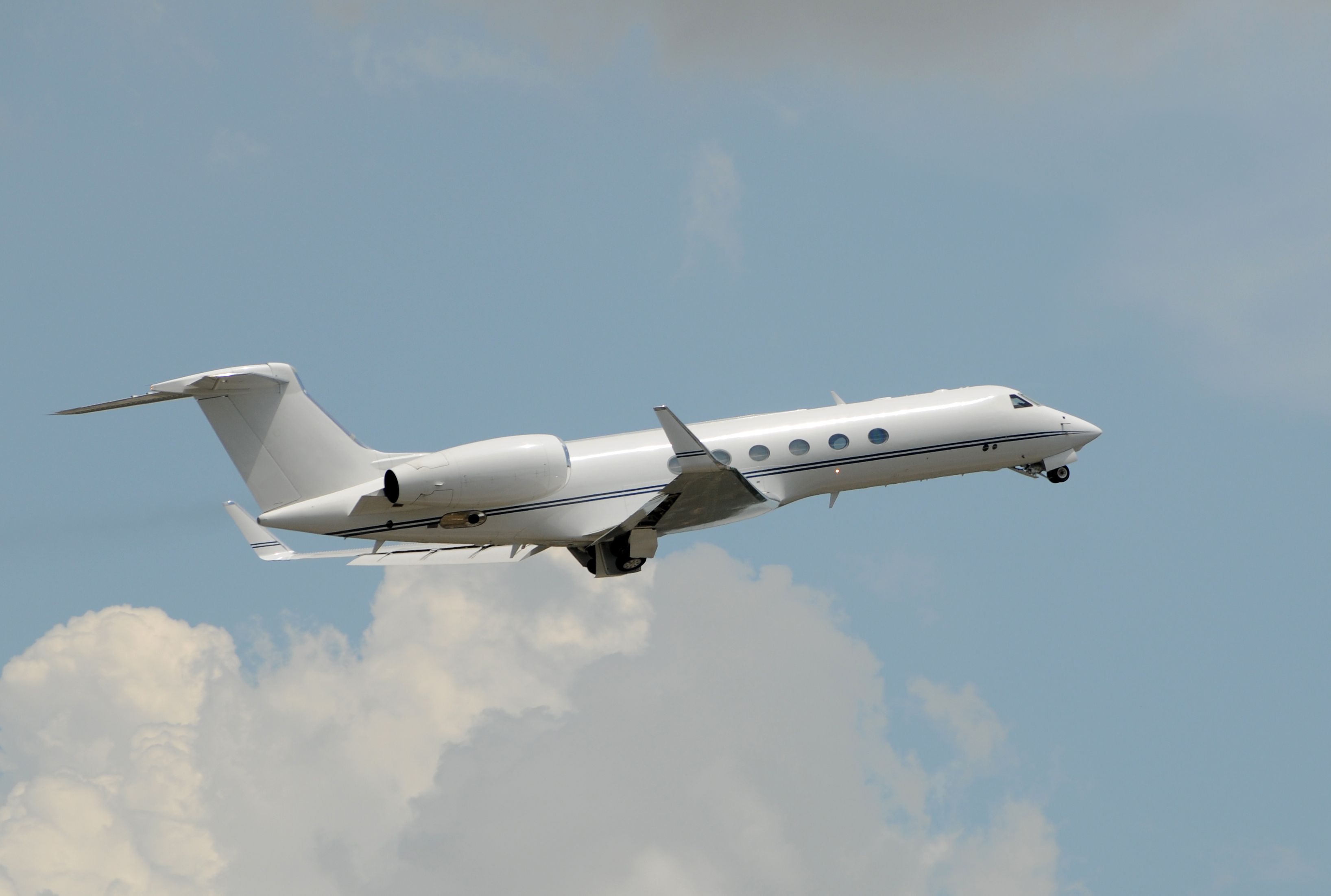 A Business jet flying in the sky while retracting its landing gear.