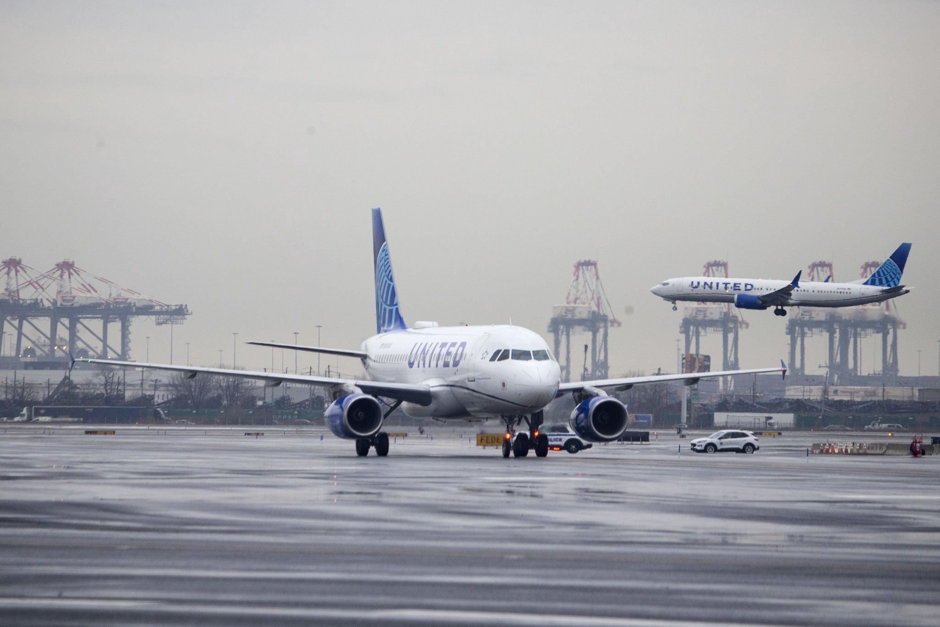 A United Airlines aircraft taxiing at Newark Airport while another lands in the background.