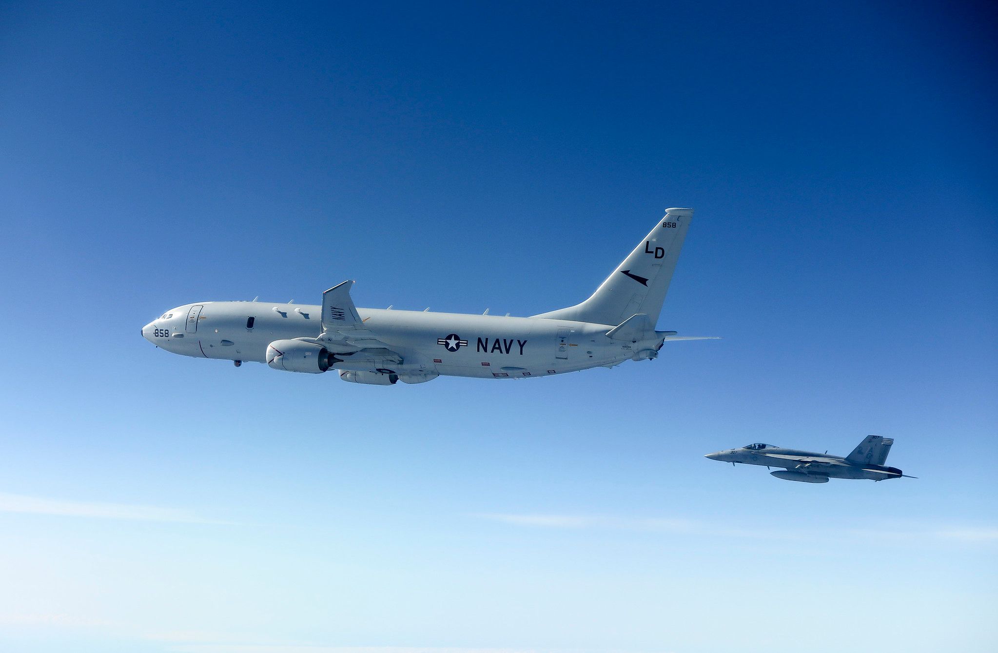 A P-8 Poseidon flying in the sky next to a fighter jet.