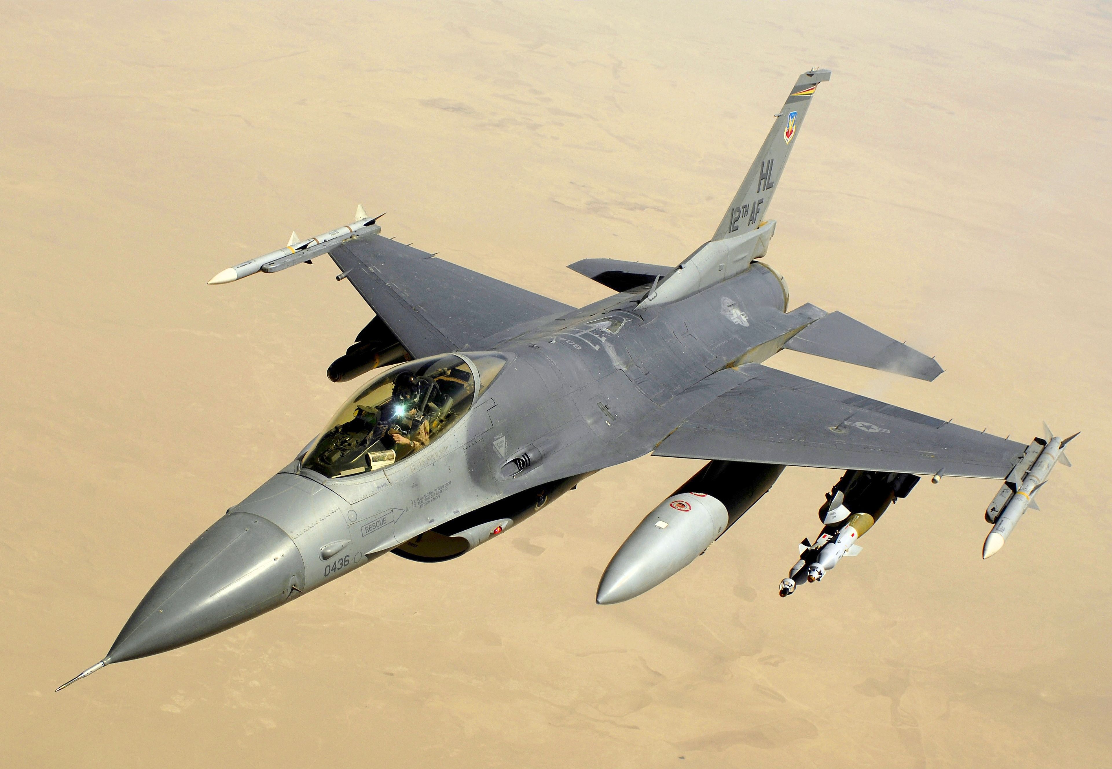 An F-16 flying over desert terrain.