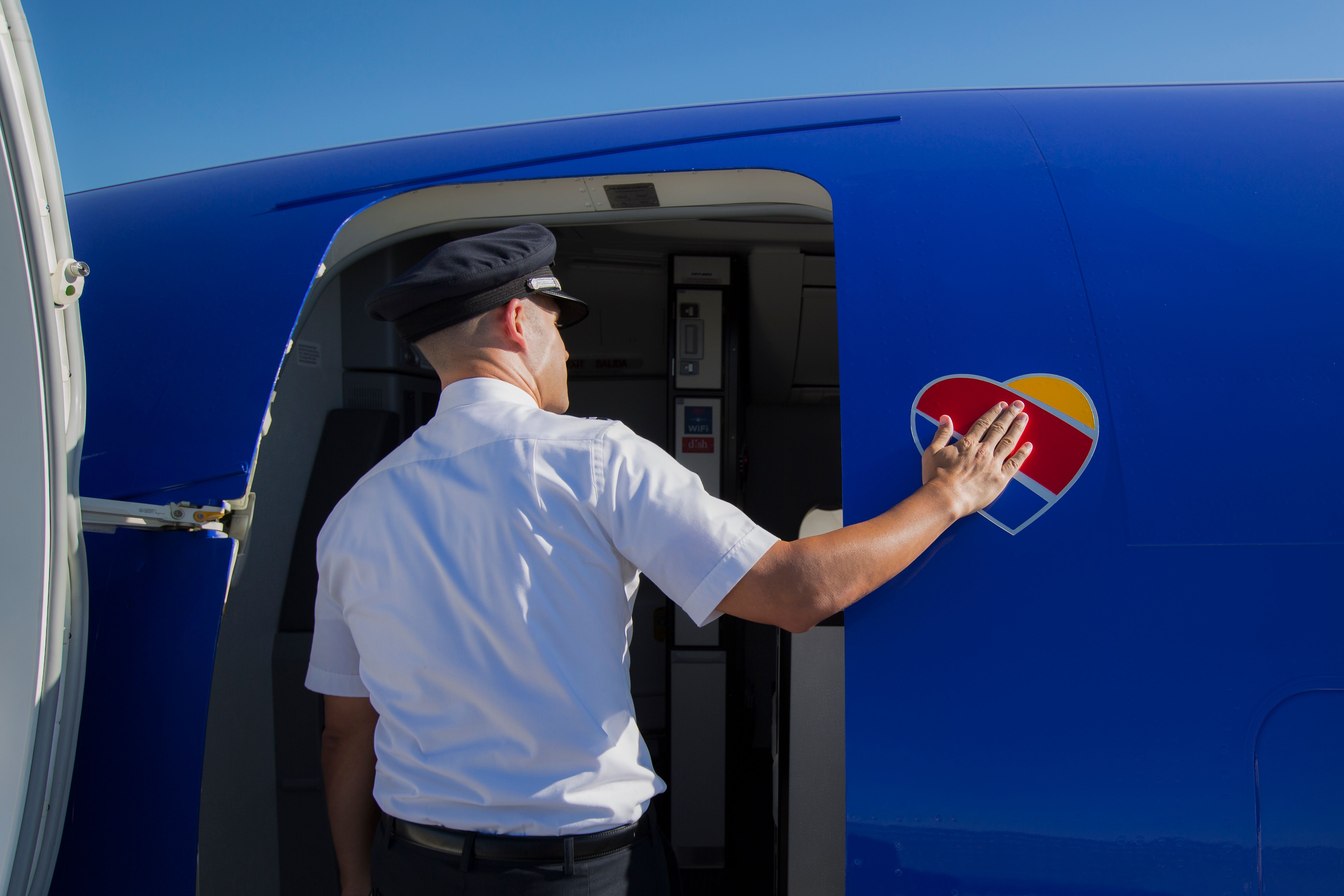 Man wearing a pilot's hat touches a heart decal as he enters a Southwest aircraft