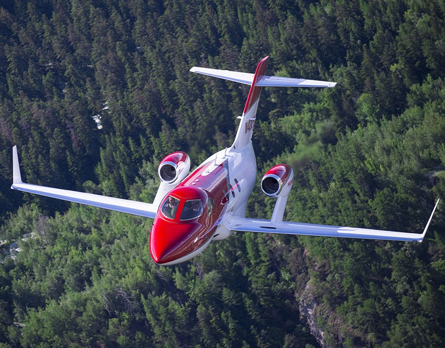 A HondaJet flying over a forest.