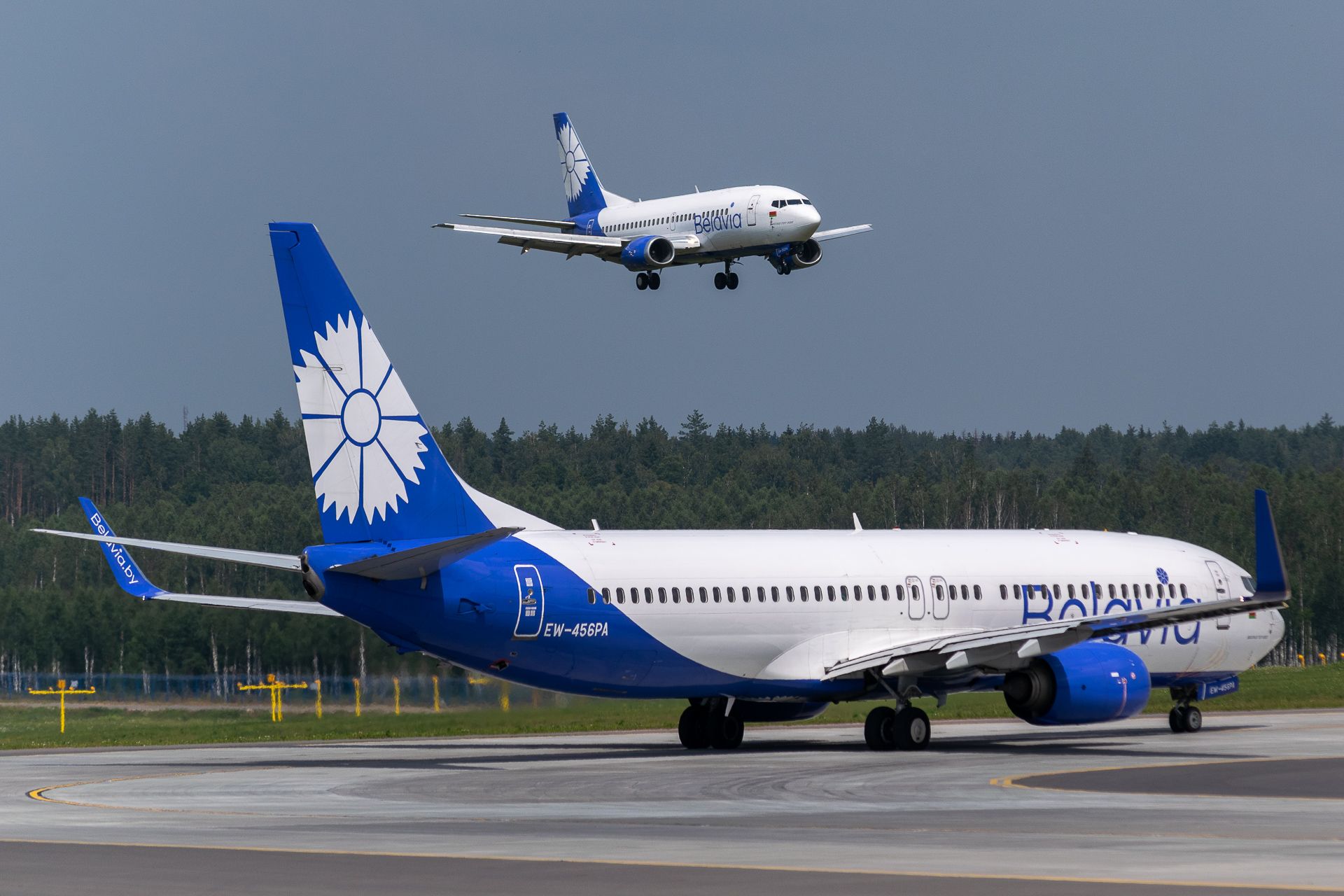 Two Belavia Boeing 737s, one about to land and the other waiting to take off.