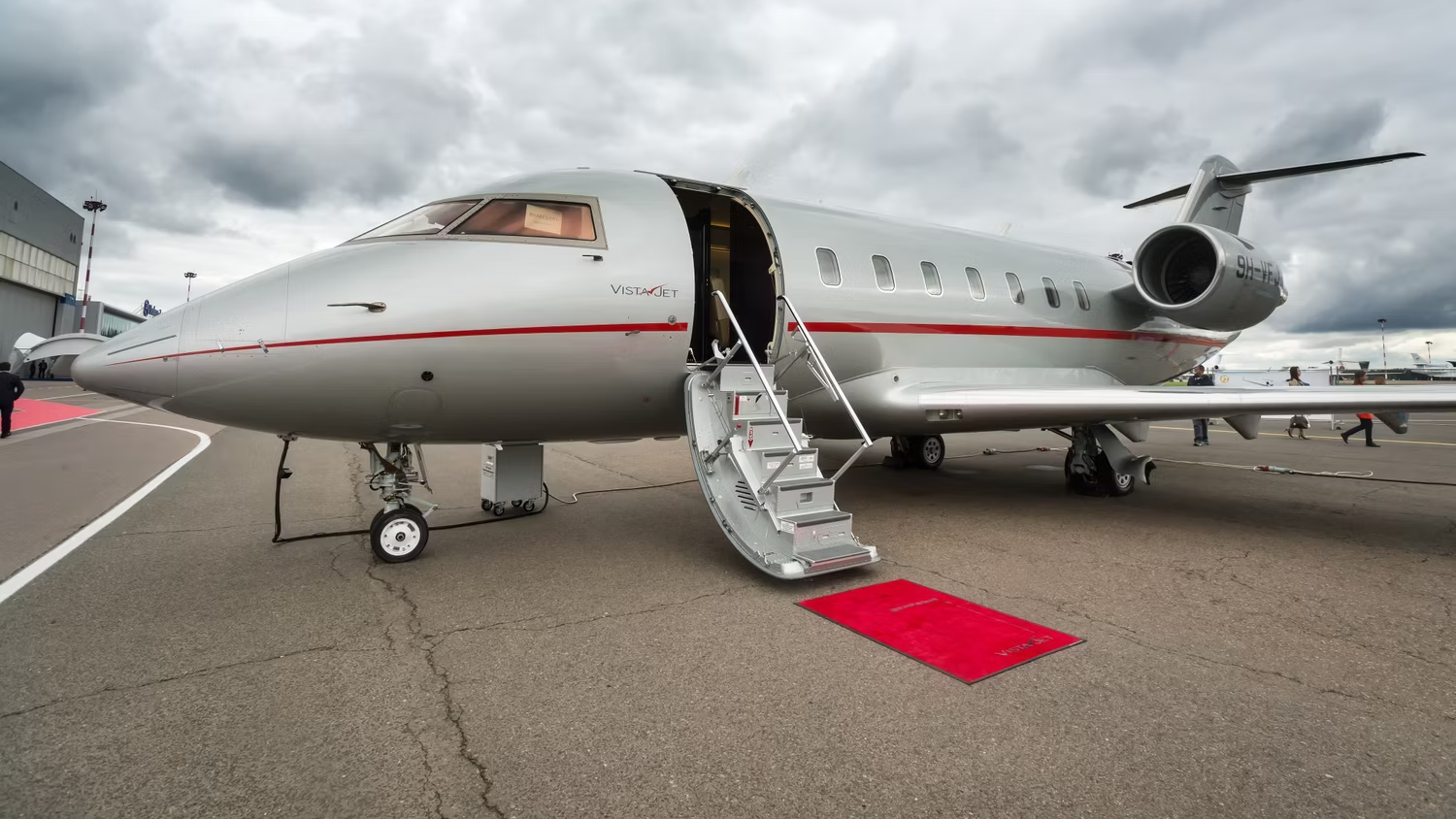 A VistaJet Bombardier Challenger Parked on an airport apron, with a red carpet leading to the aircraft stairs.