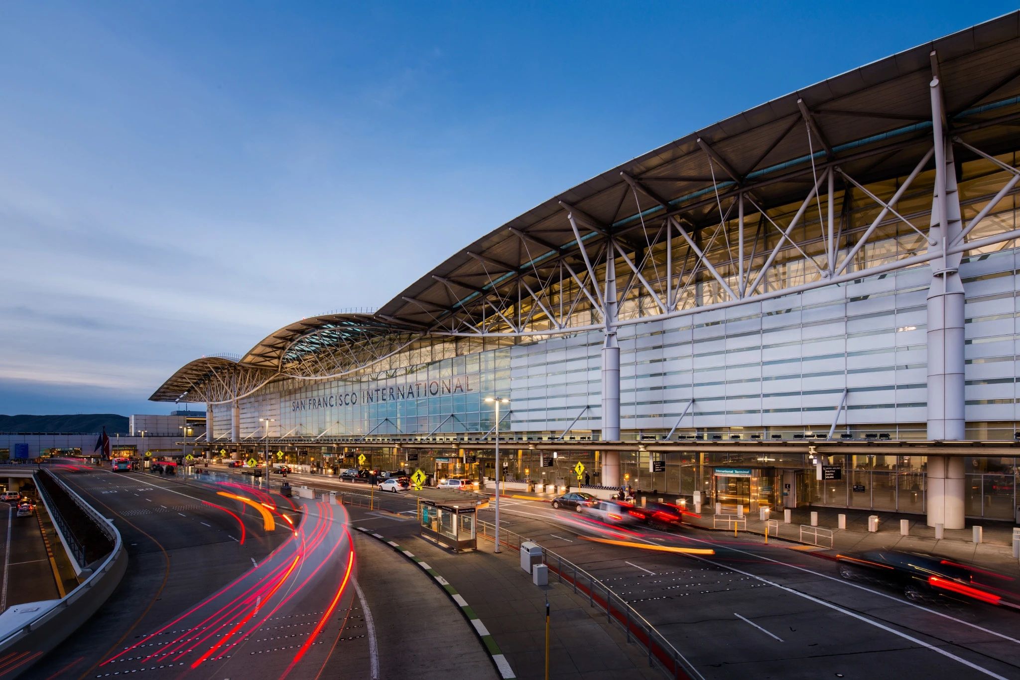 Street view of San Francisco International Airport passenger terminal at dusk with vehicles parked in front