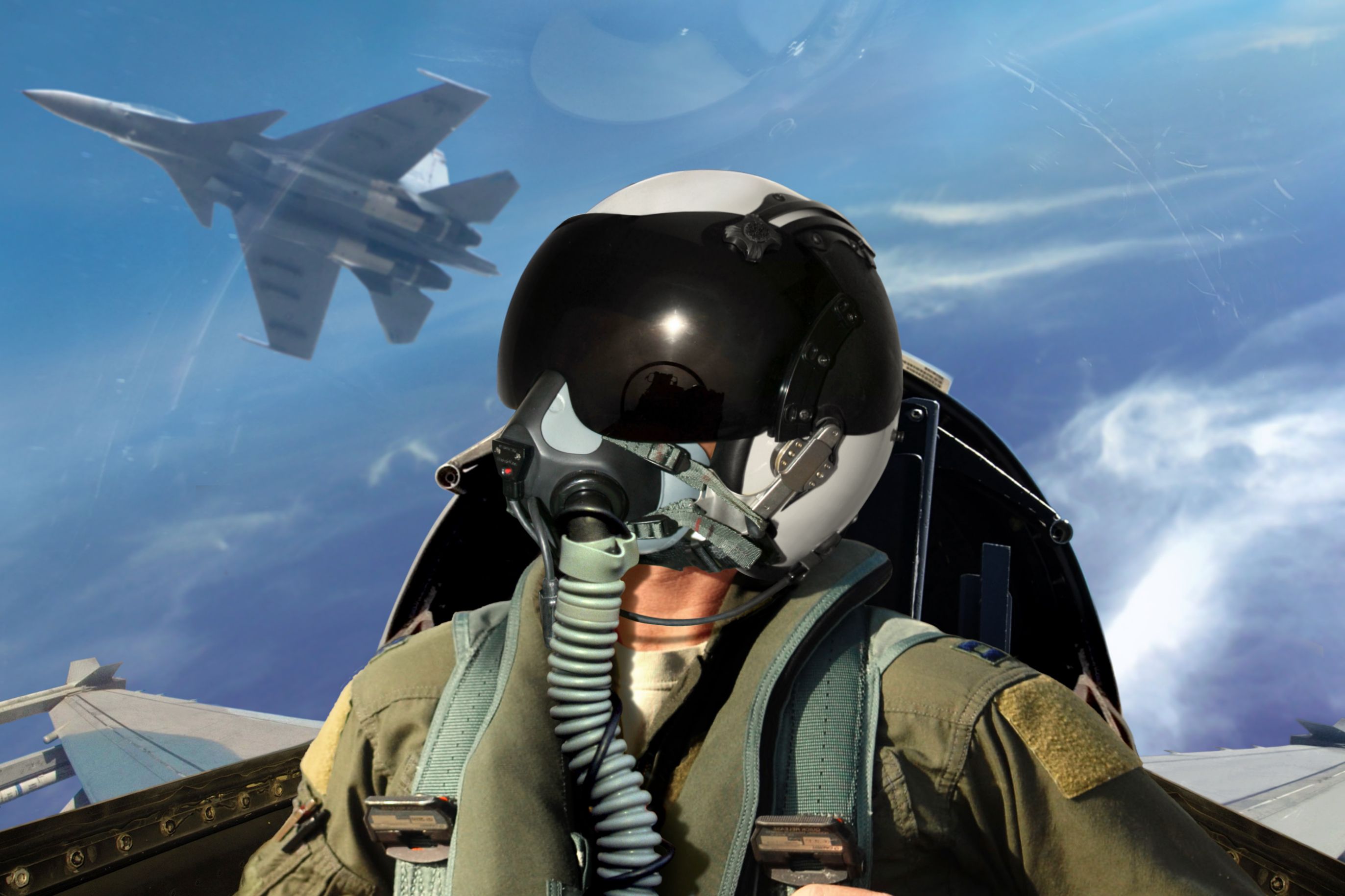 A Fighter pilot wearing a mask, with another fighter jet flying just behind him.
