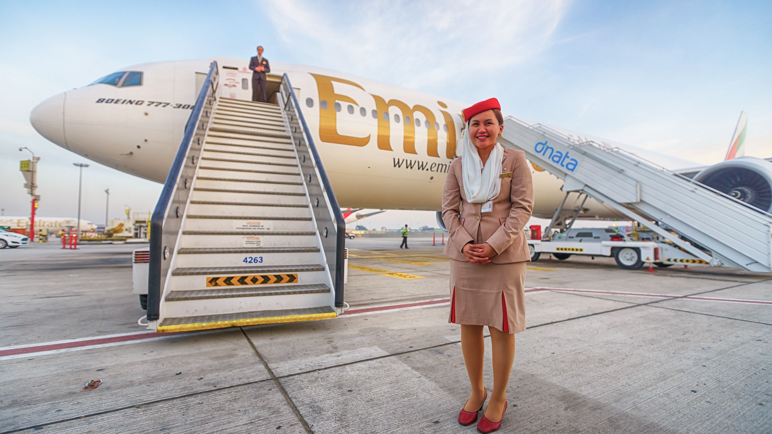 A flight attendant stands nearby an Emirates Boeing 777.