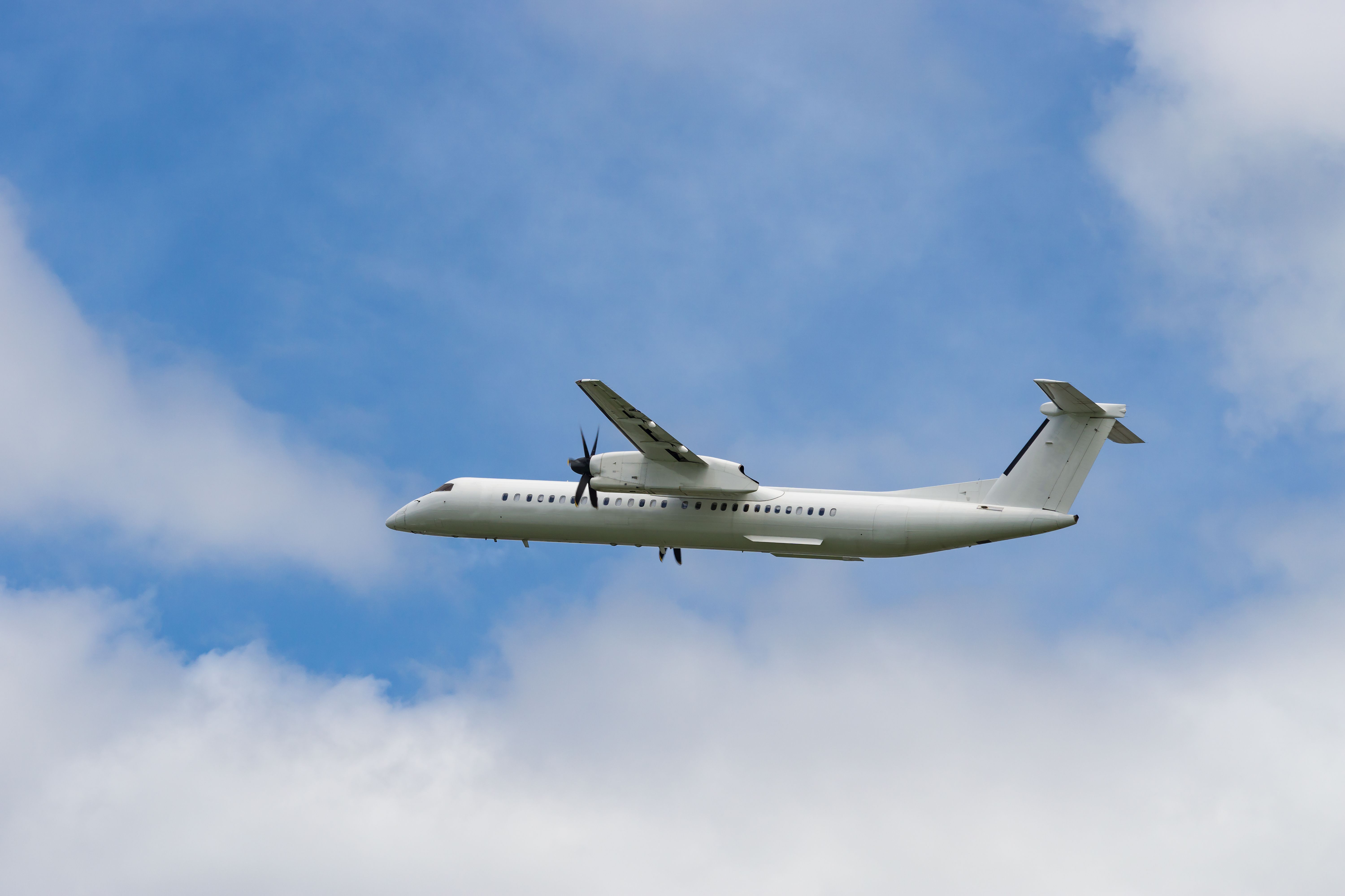 White Dash 8 turboprop aircraft taking off from airport. 