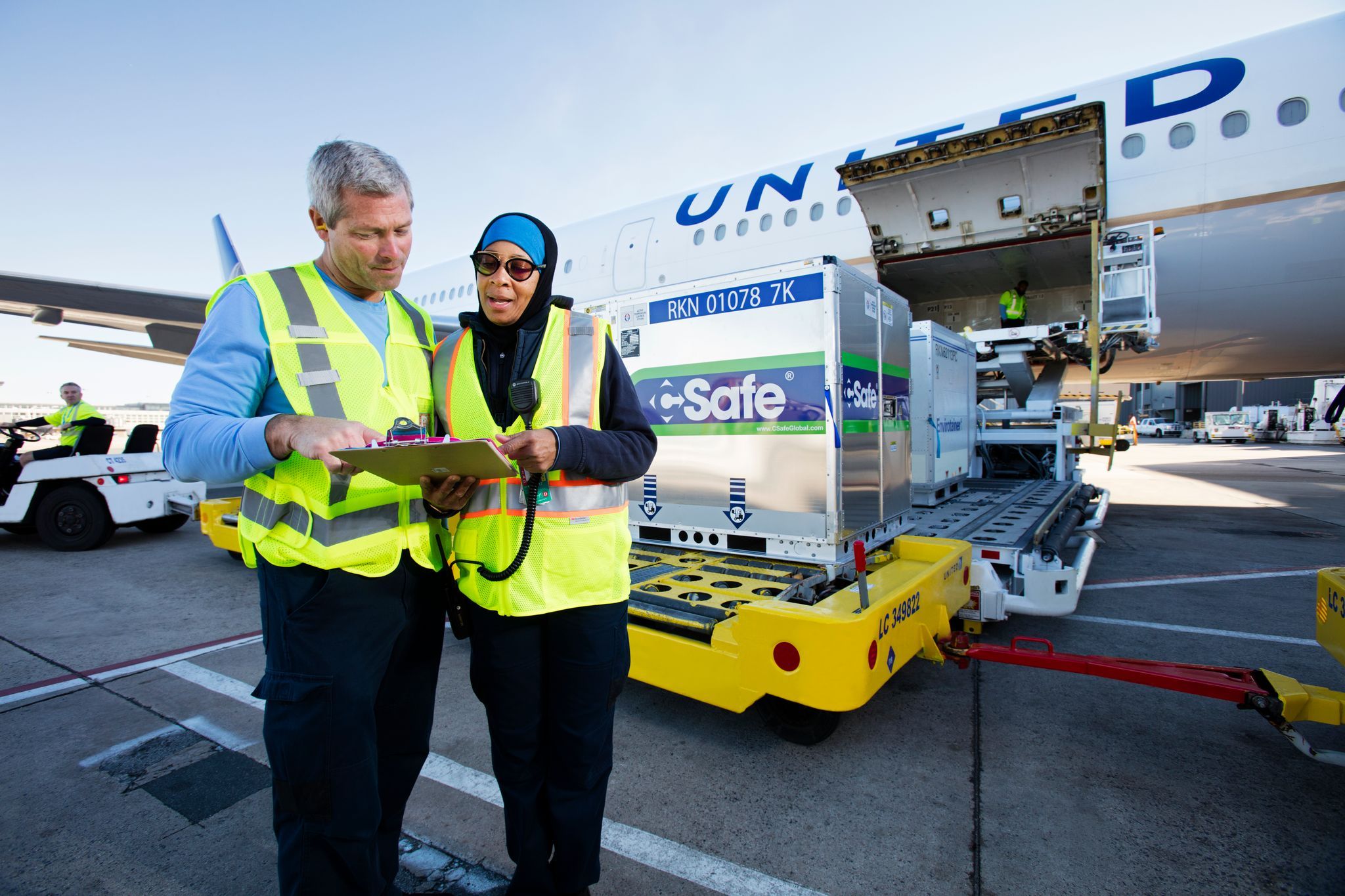 Two employees wearing yellow safety vests look over a clipboard next to a United Airlines aircraft.