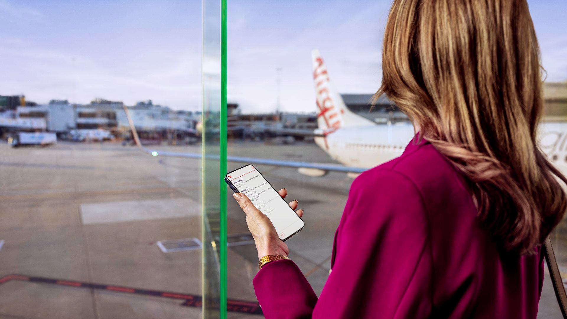 A woman looking at a Virgin Australia aircraft from a terminal window.