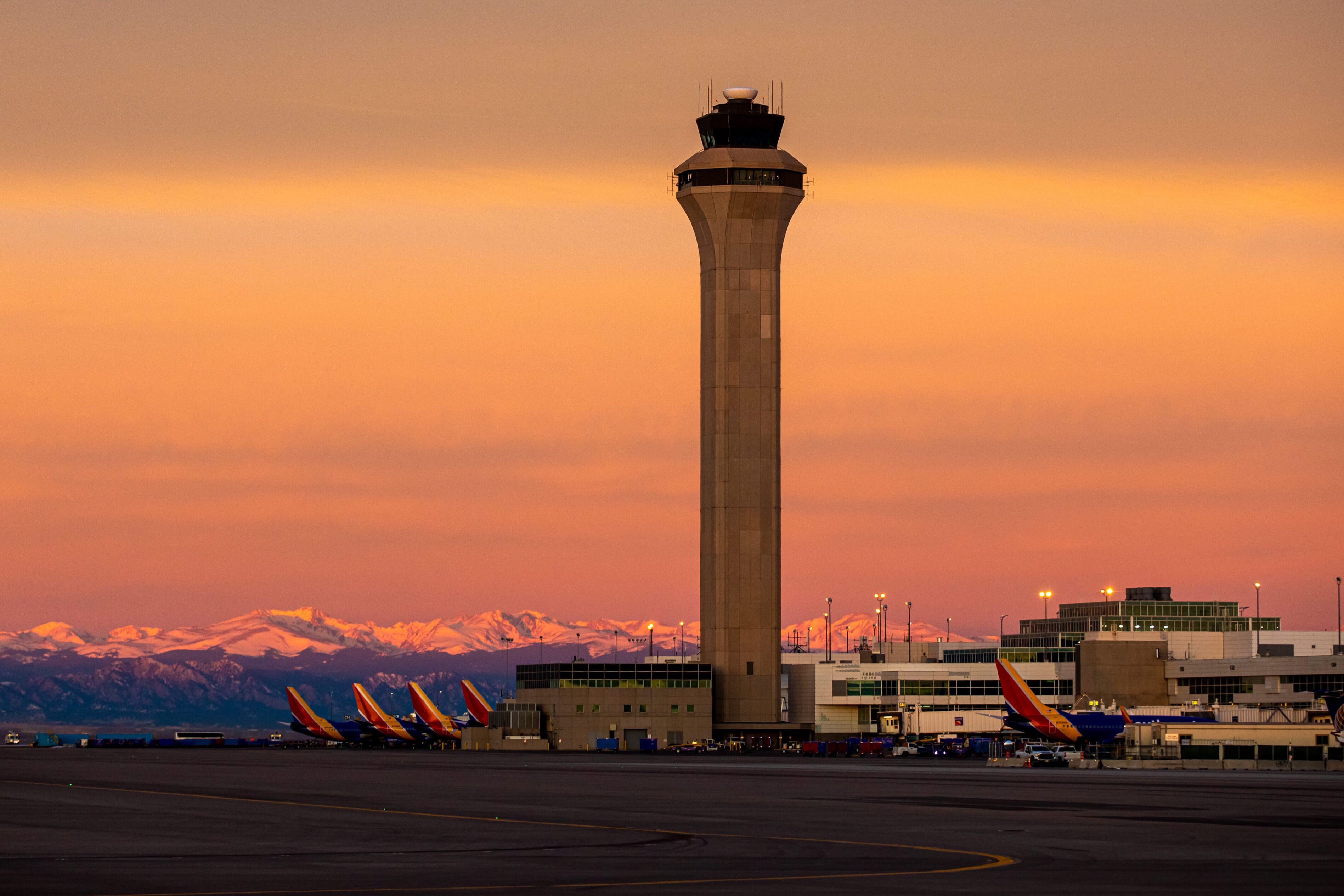 An ATC tower and several Southwest Airlines aircraft at Denver International Airport during sunrise.