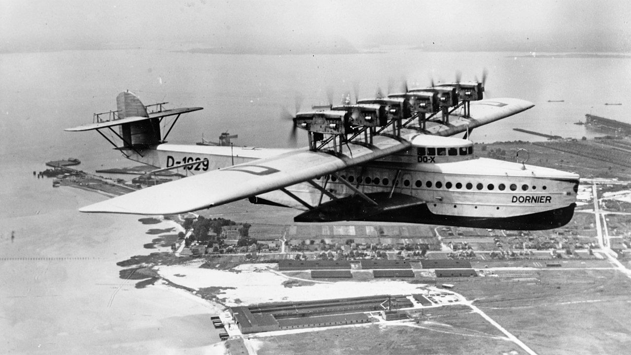 A Dornier Do X flying over a coastal area.