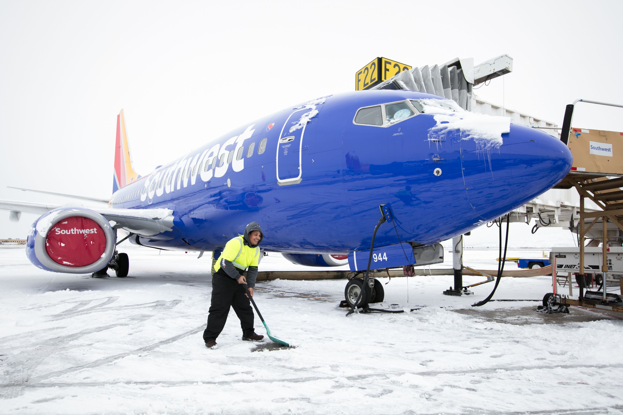 A ground crew member in a bright green safety jacket sweeps snow away from the ground near a Southwest Airlines aircraft.