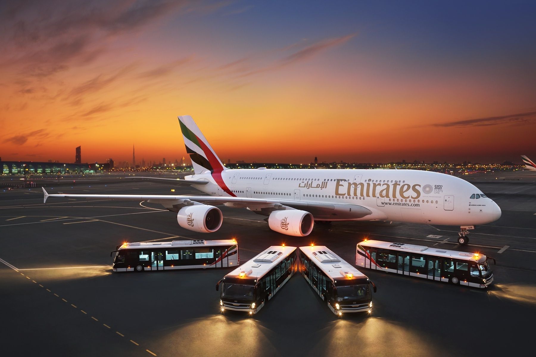 An Emirates A380 parked next to four Emirates buses.