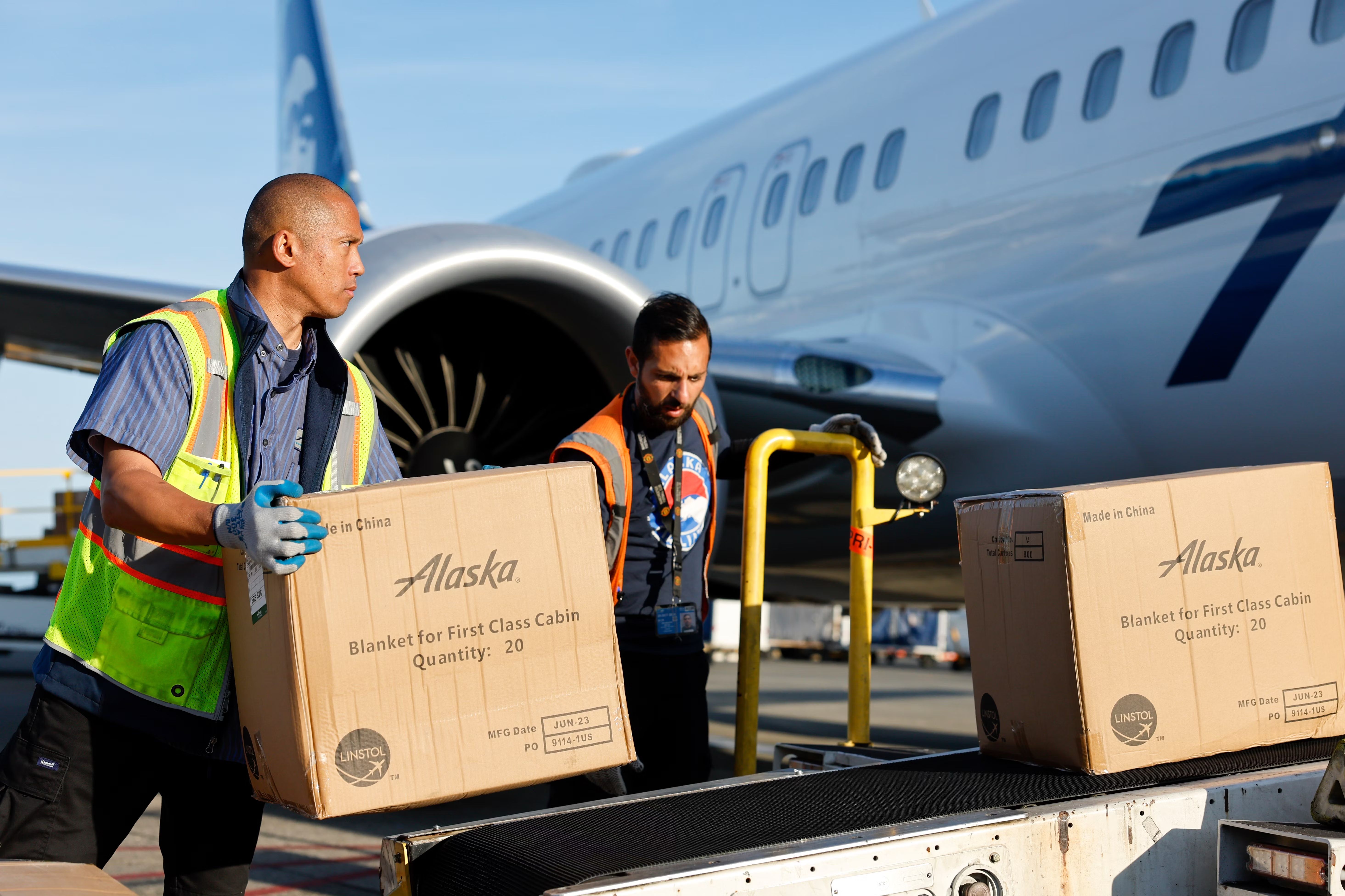 Alaska Airlines workers load cargo boxes onto an aircraft.