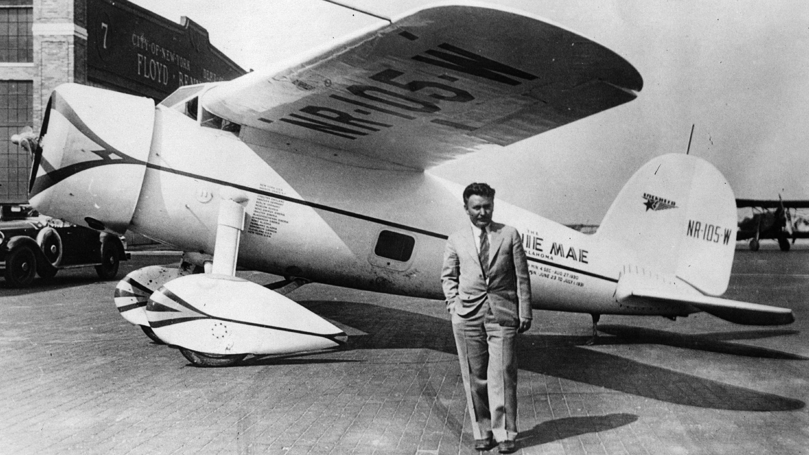 A black and white photo of Wiley Post standing near an aircraft.