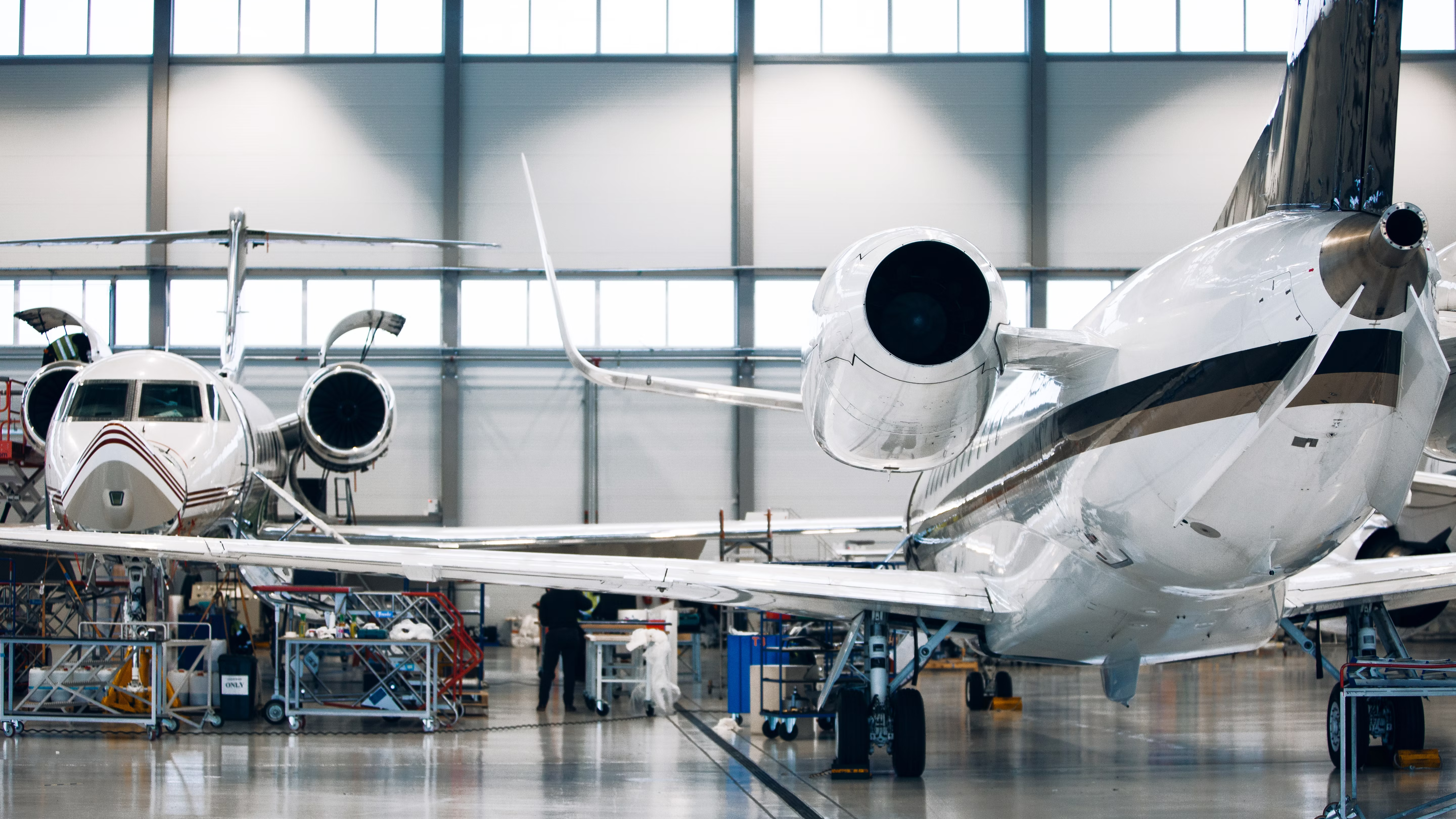 Engineers working on two private jets in large white hangar.