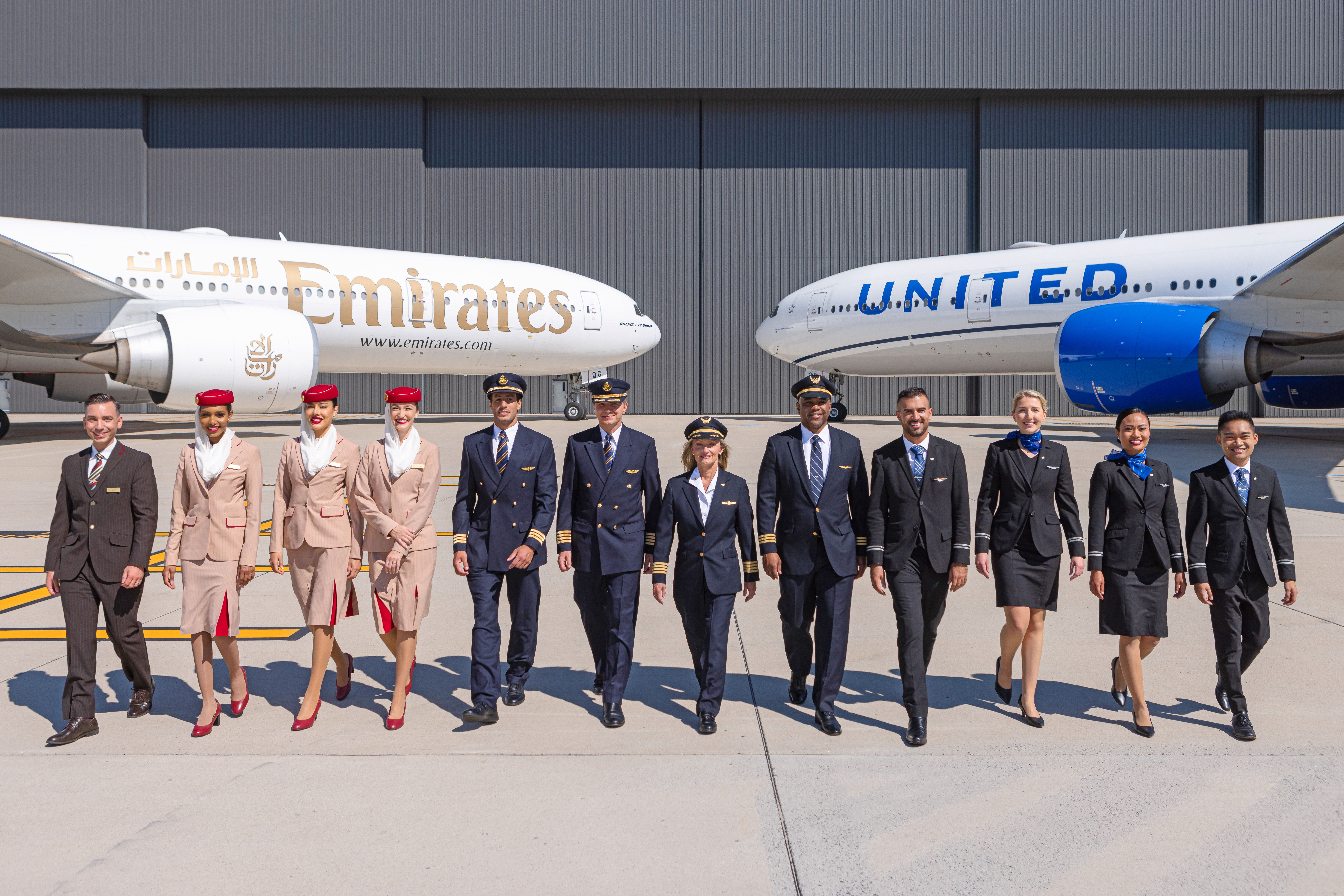 Emirates and United Airlines aircraft parked side by side near a hangar, with cabin crew from both airlines standing together.