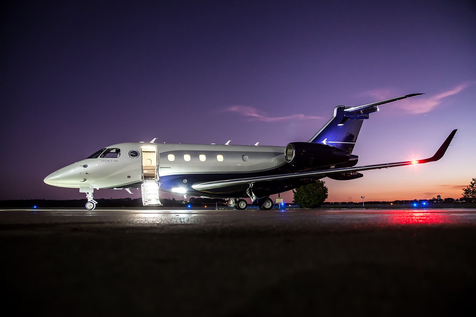 An Embraer Legacy 450 parked at an airport at night.