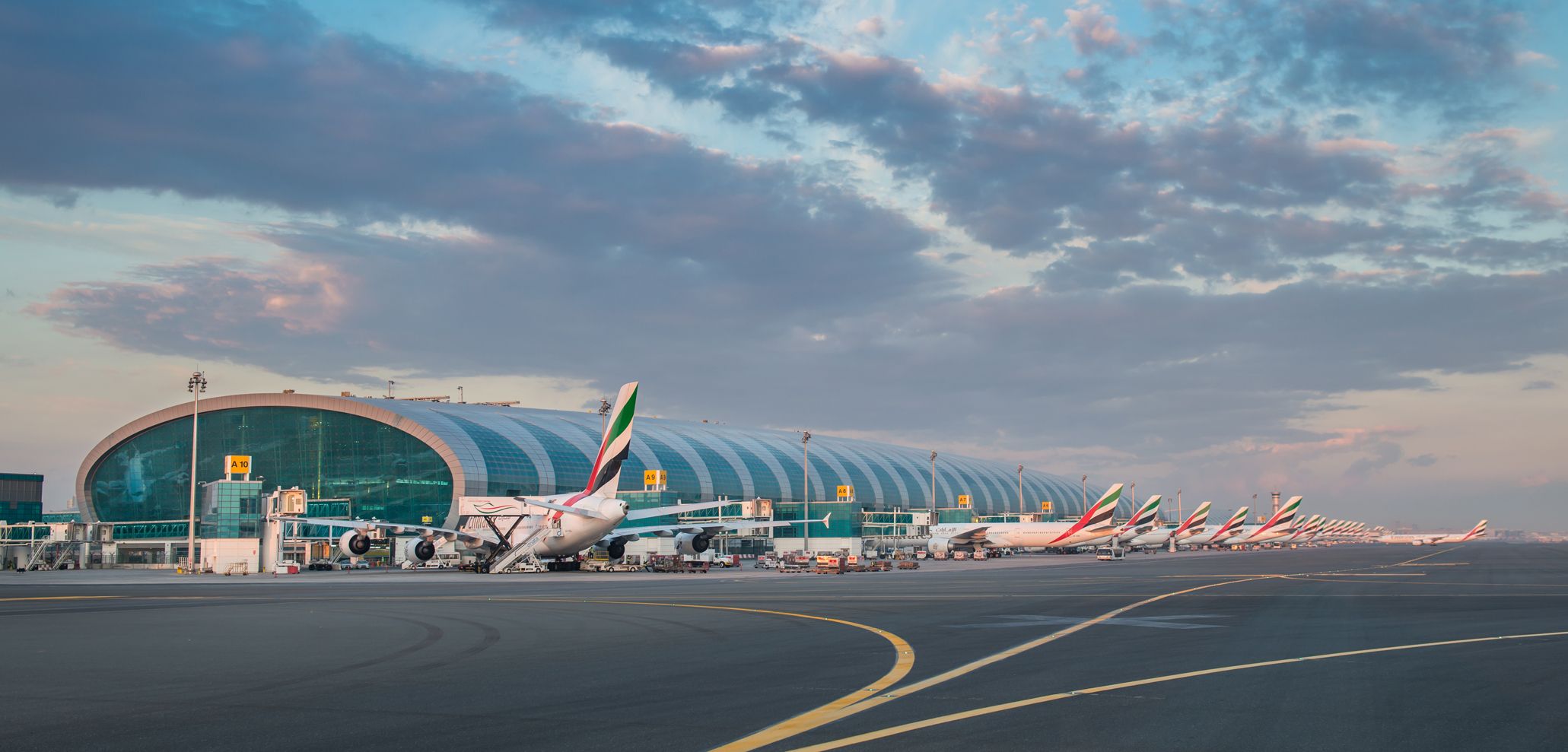 A Panoramic view of Dubai International Airport with several Emirates aircraft parked at gates.
