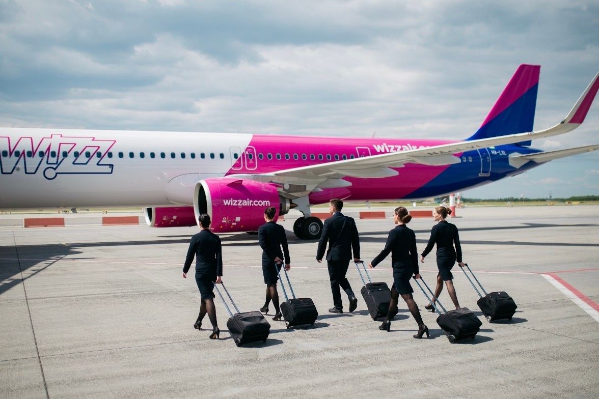 Five Wizz Air cabin crew members walking towards the aircraft.