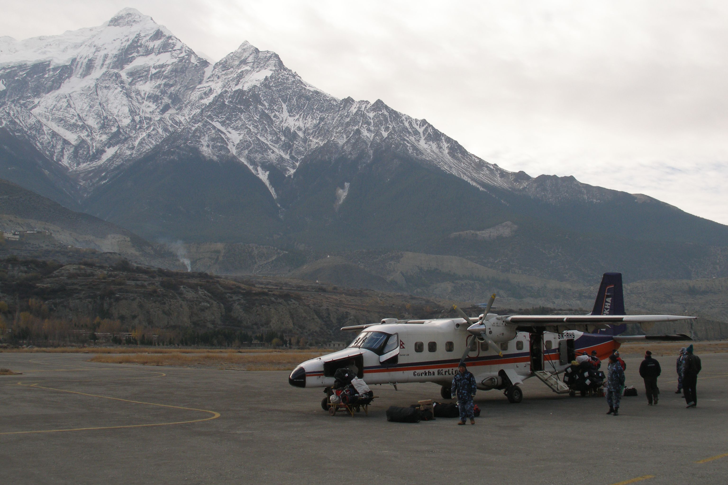 A small aircraft parked at an airport with the Himalayan mountians in the background.