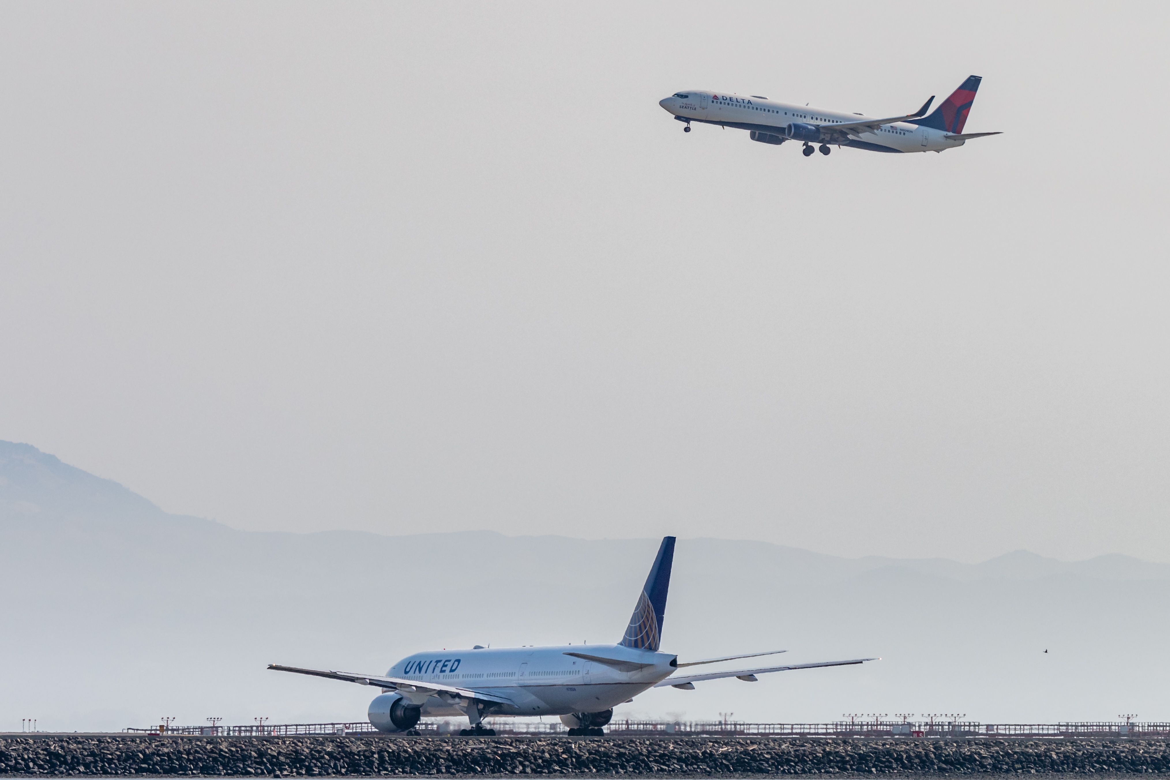A United Airlines aircraft on the ground and a Delta Air LInes aircraft flying in the sky.