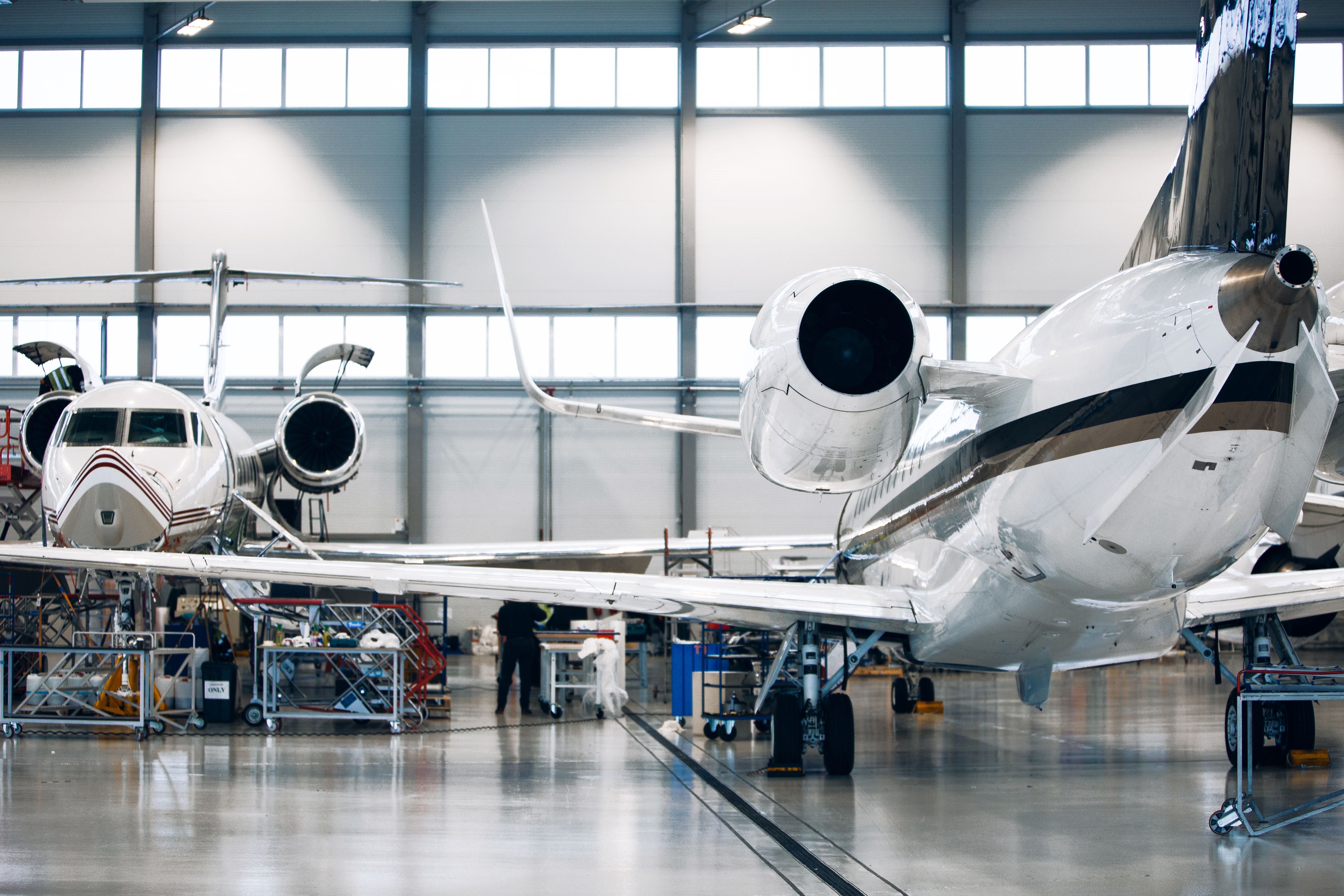 Engineers working on two private jets in large white hangar.