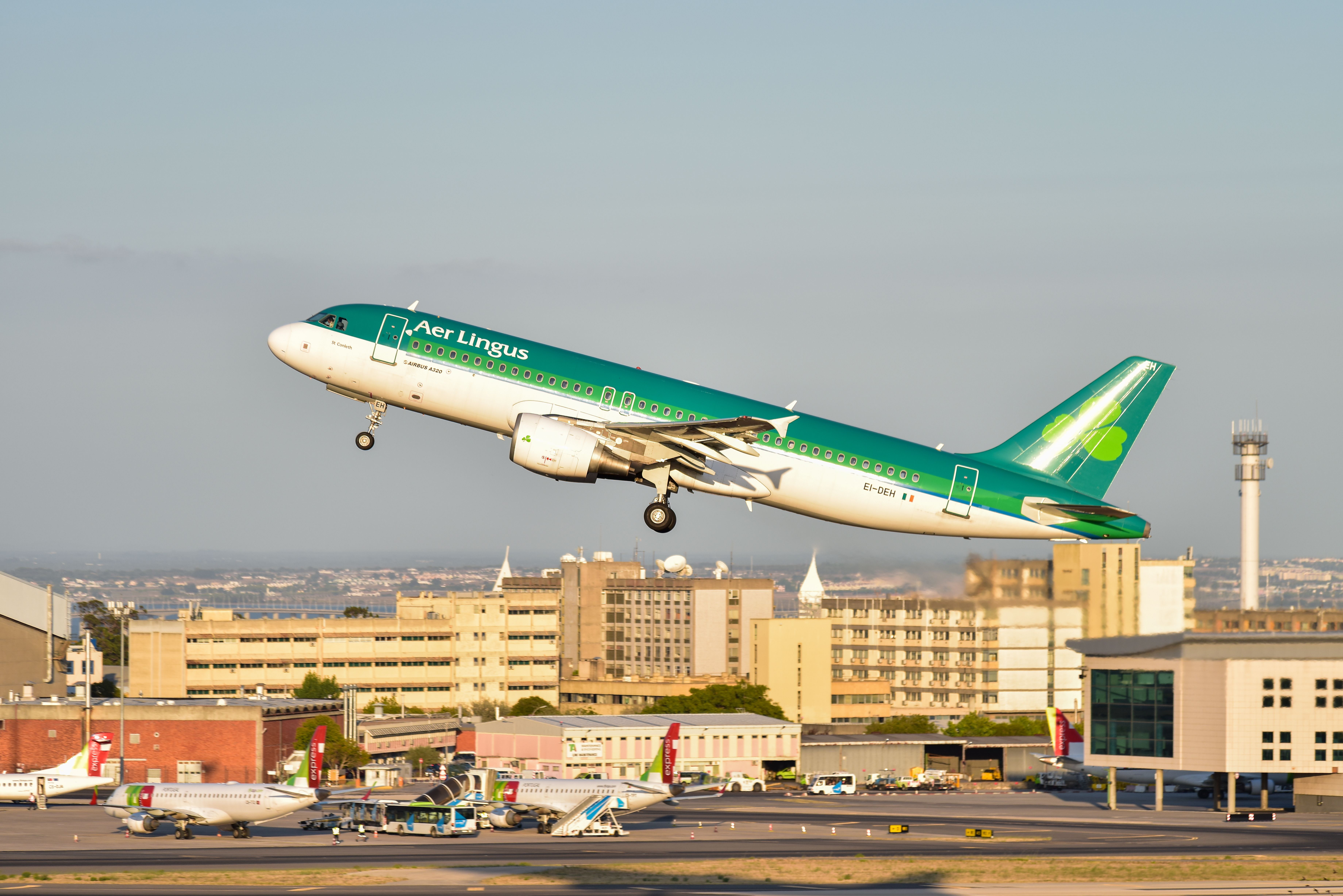 An Aer Lingus Airbus A320 -214 lands at Lisbon Airport in front of TAP Air Portugal planes and the air traffic control tower