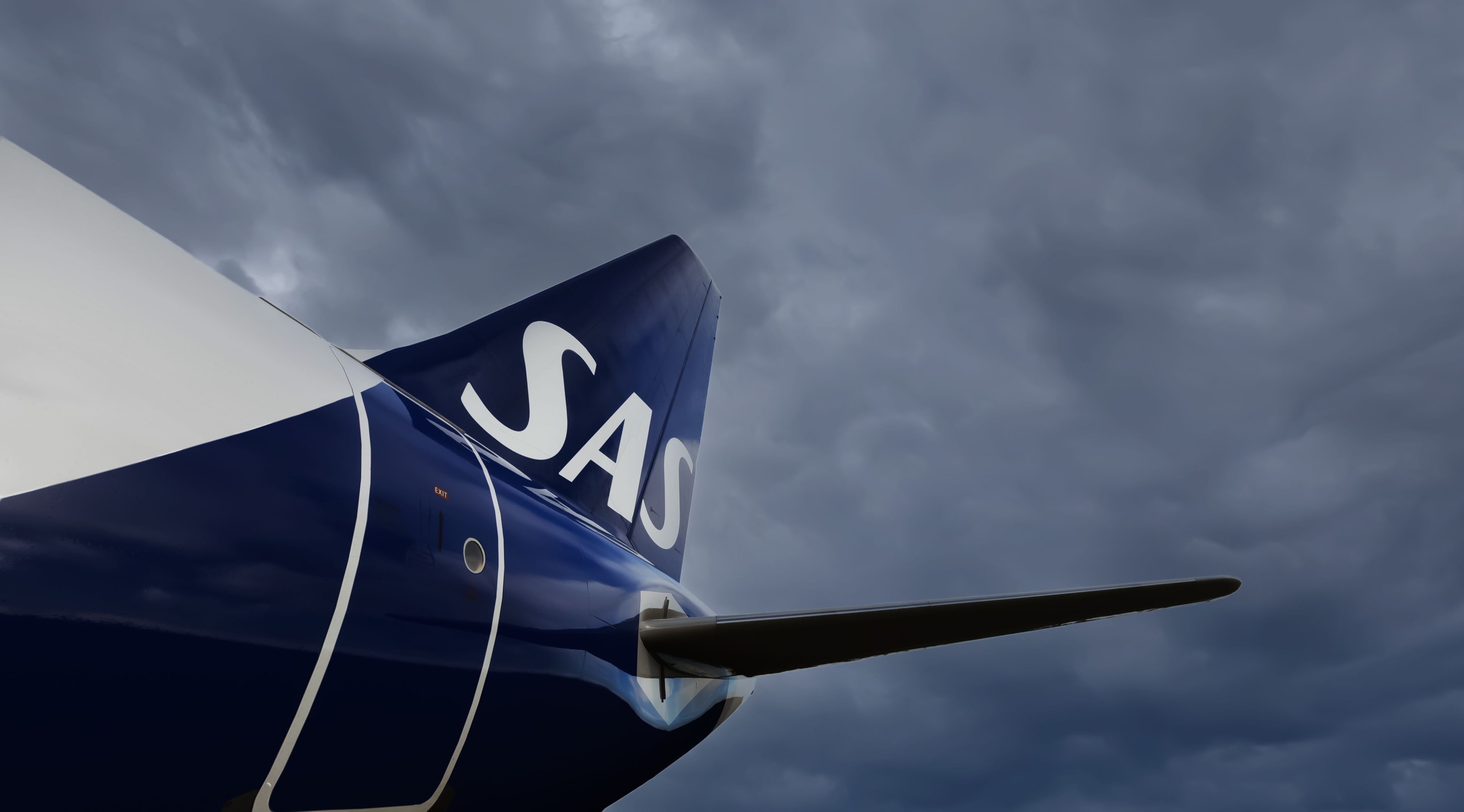 shutterstock_2200636453 - Copenhagen, Denmark - Sep. 10th 2022: Tail of a jet airliner with the SAS logo or Scandinavian Airlines. Dark grey clouds in the background.