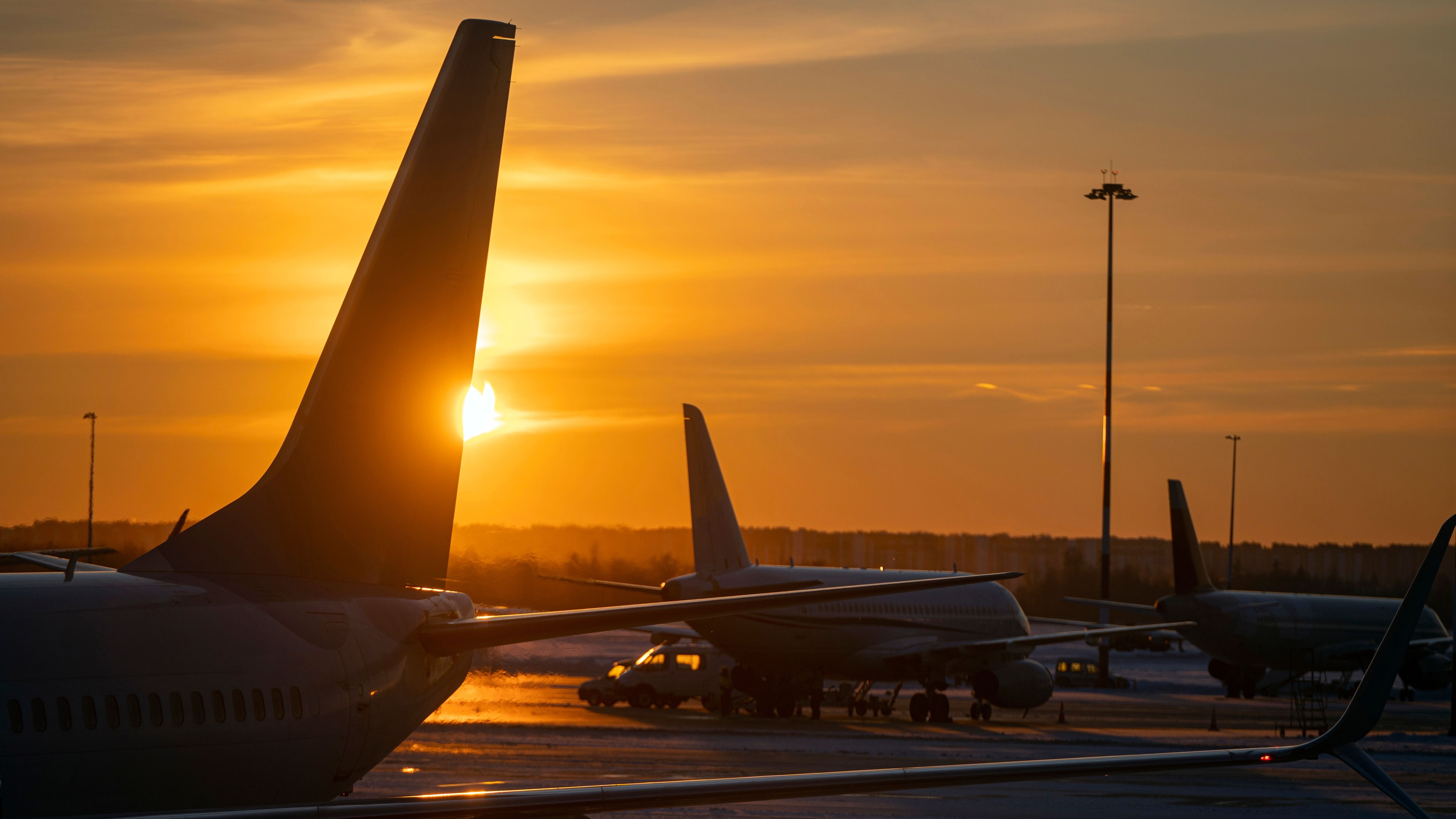 Silhouettes of the airplanes with Tails at airport during bright yellow sunset, concept picture about transport as background.