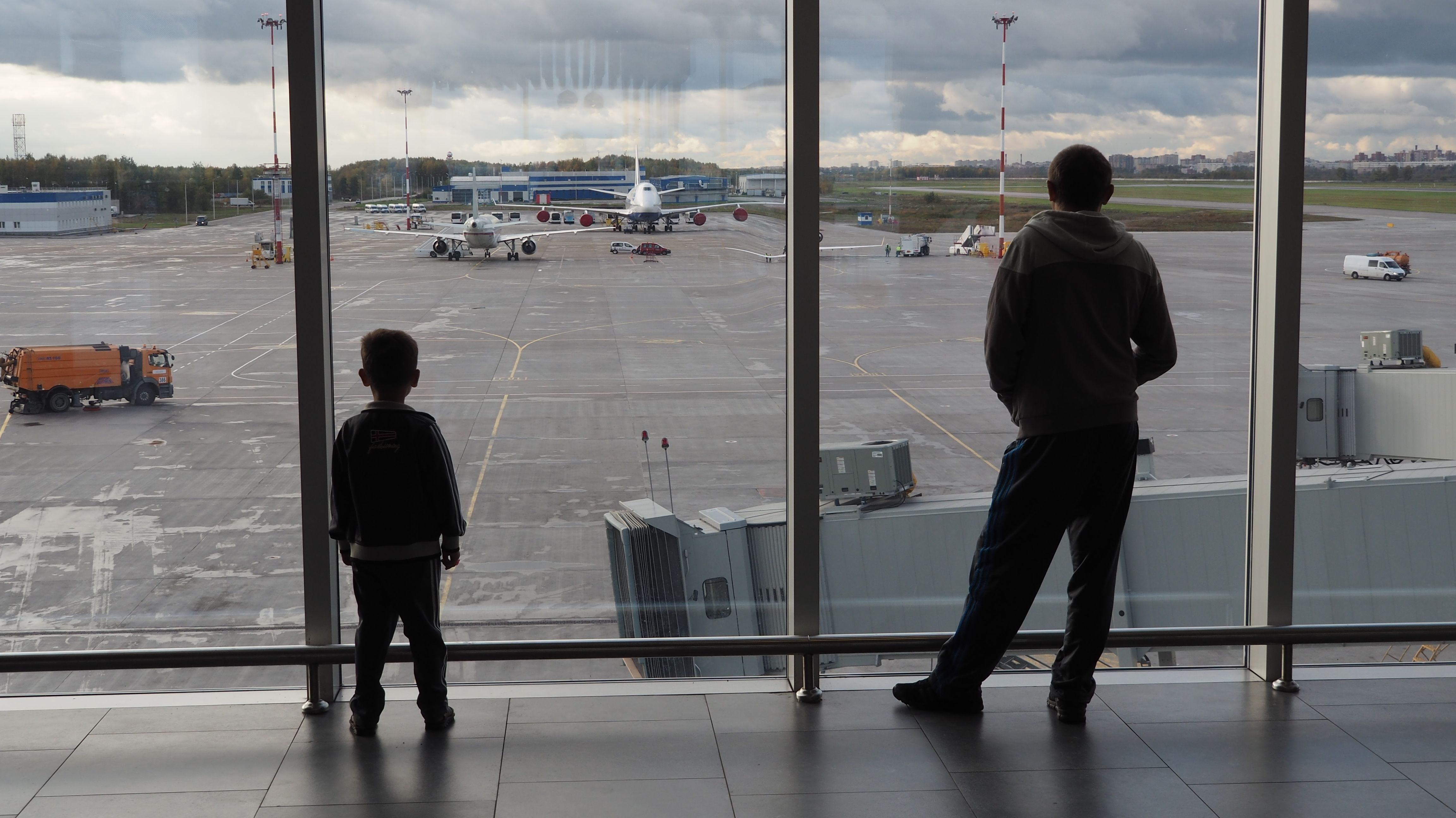 A Passenger and a child looking at some aircraft from an airport terminal window.