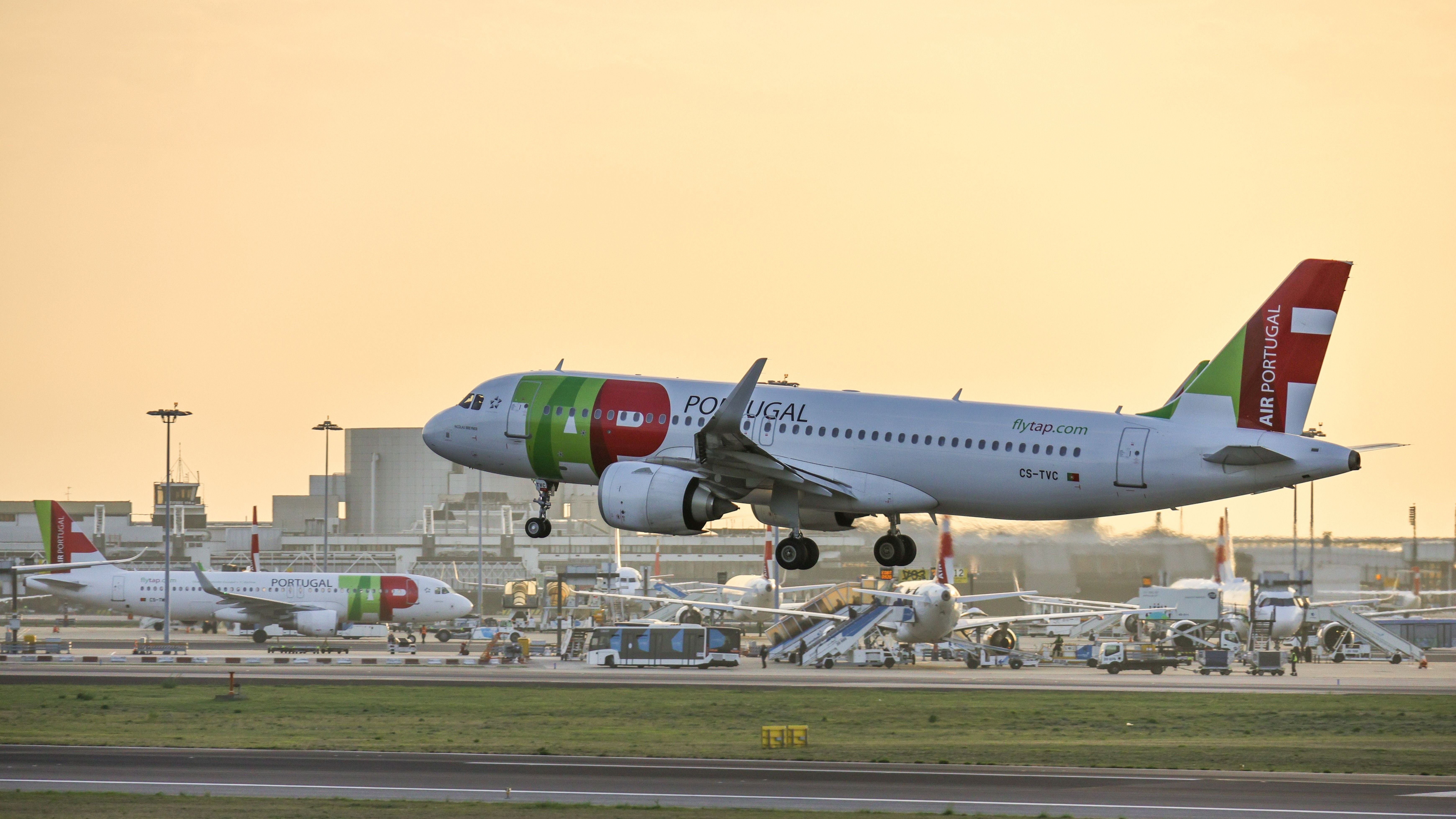 A side view of a TAP Air Portugal airplane departing from Humberto Delgado Airport at sunset.