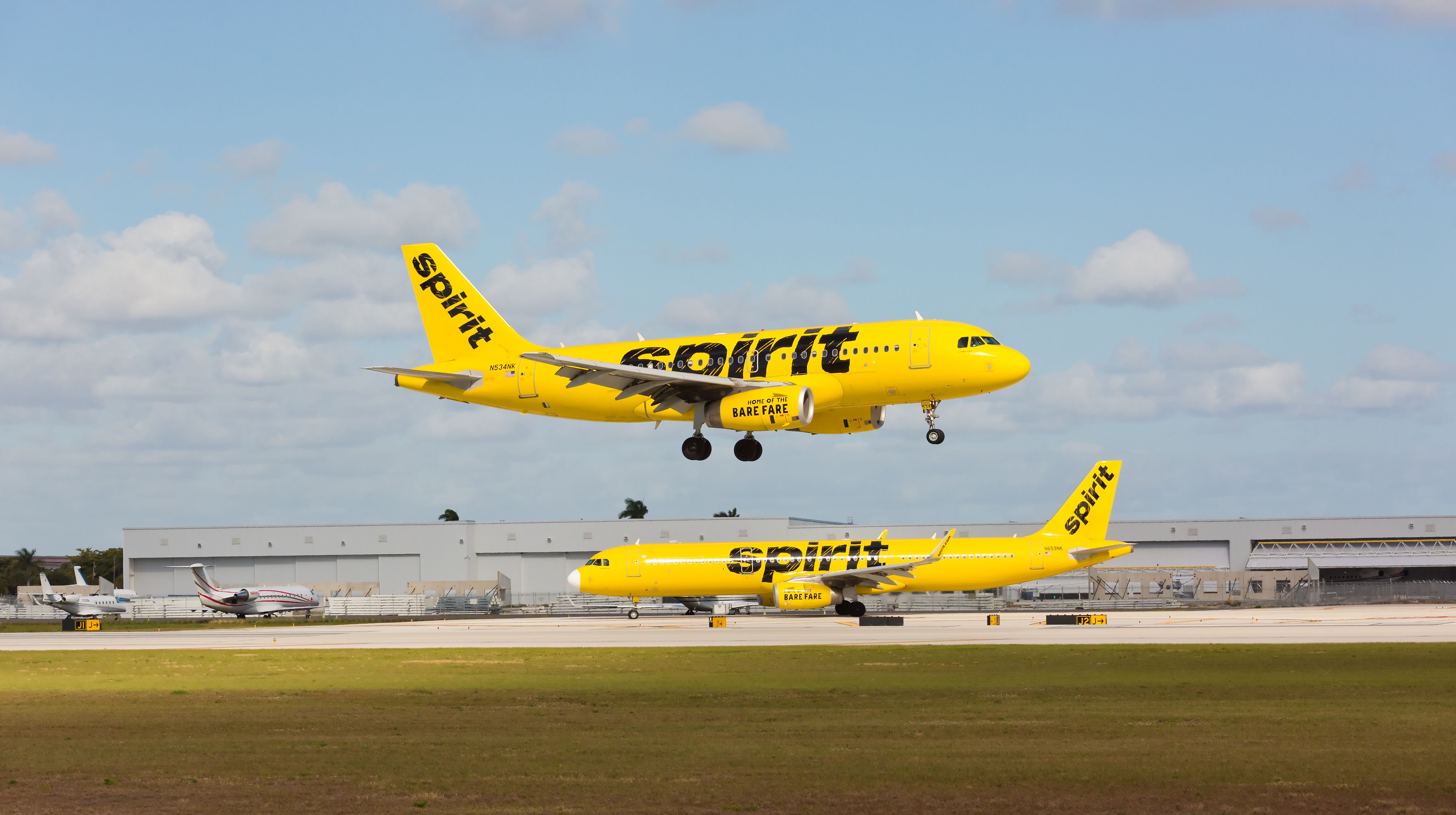 A Spirit Airlines A319 landing at Fort Lauderdale/Hollywood International Airport, while another waits to take off.