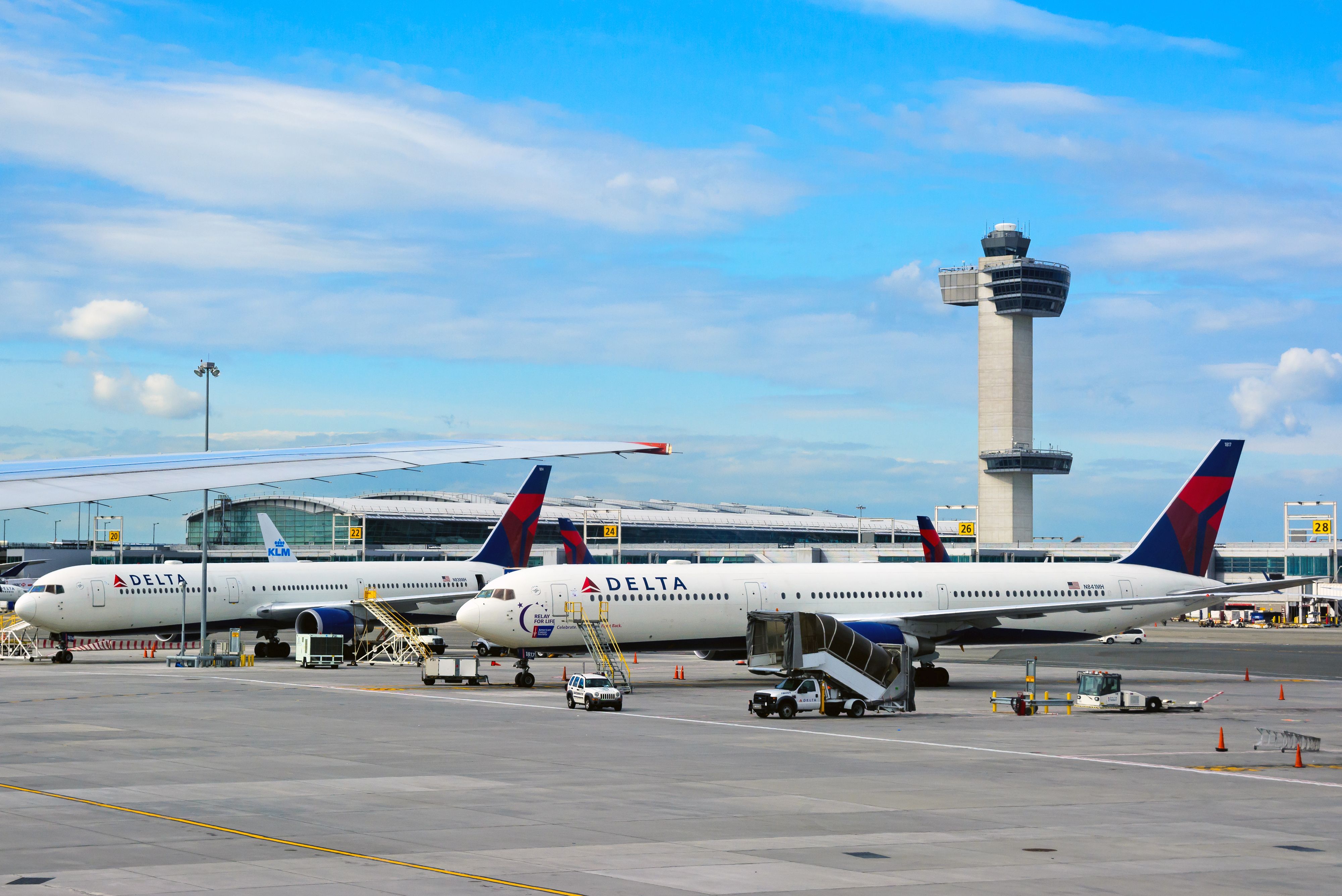 A view of the apron at John F. Kennedy International airport with multiple parked Delta Air Lines' planes and the control tower in background.
