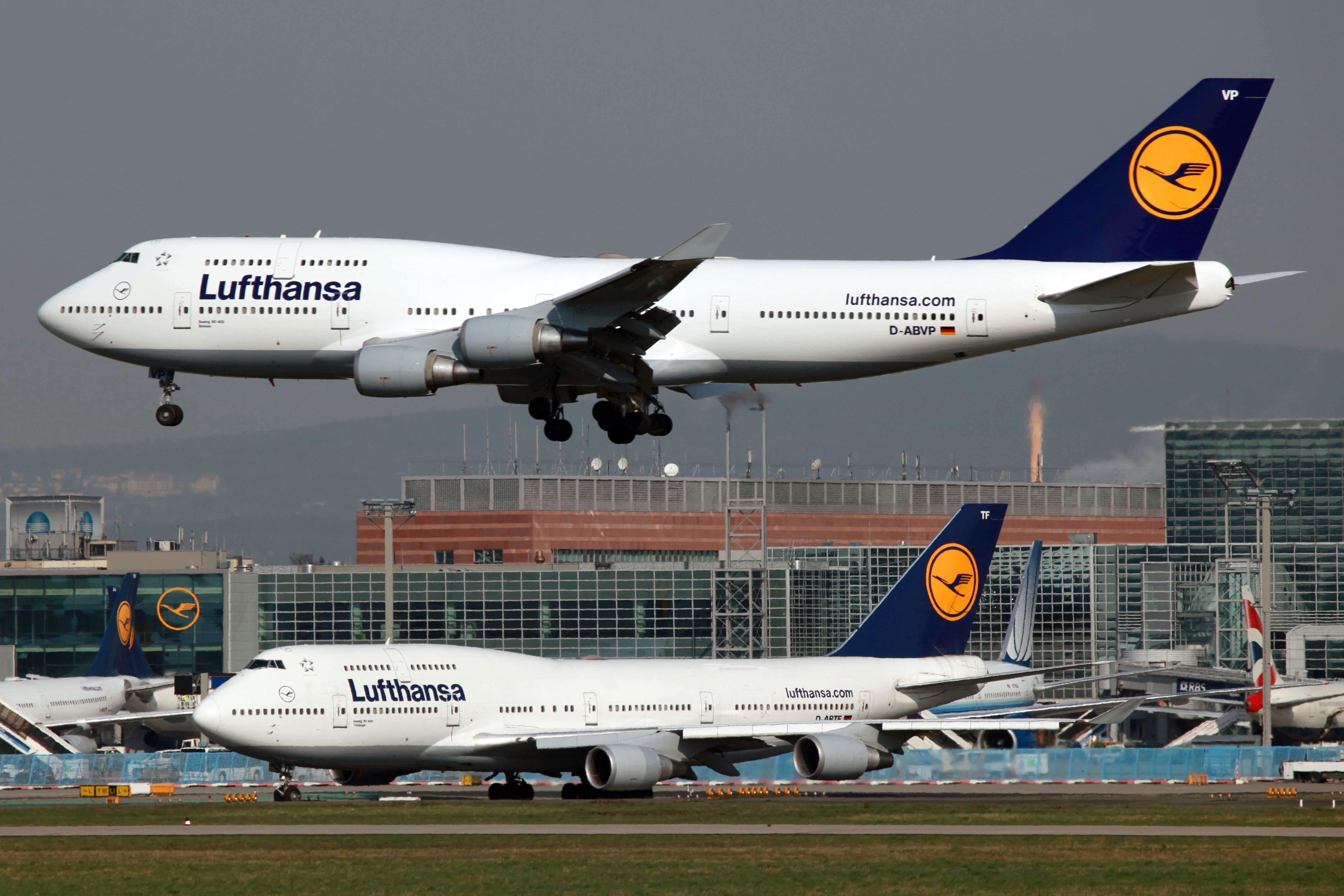 Two Lufthansa Boeing 747s, one taxiing while the other is about to land.