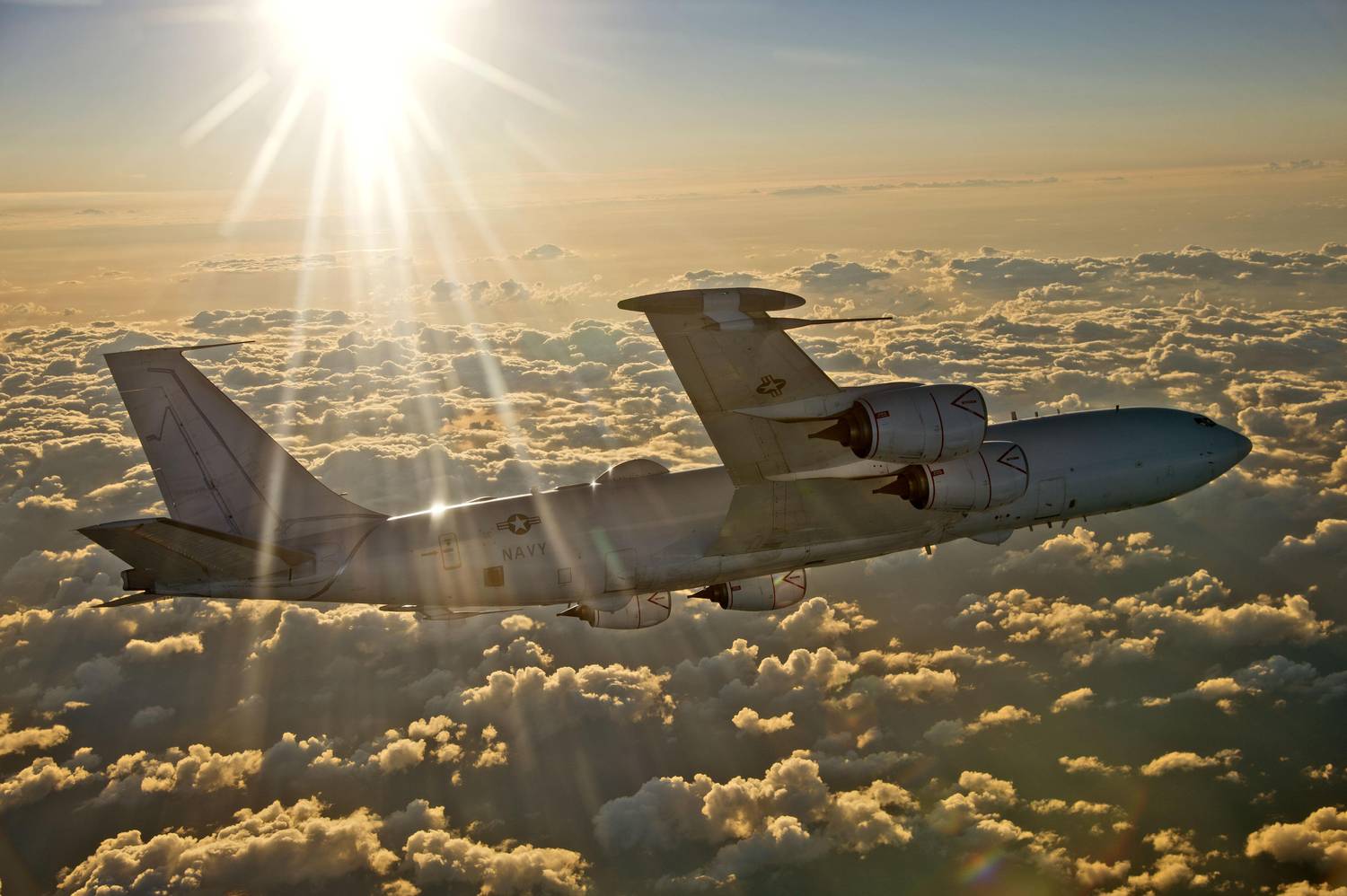 A US Navy Boeing E-6B flying over clouds.
