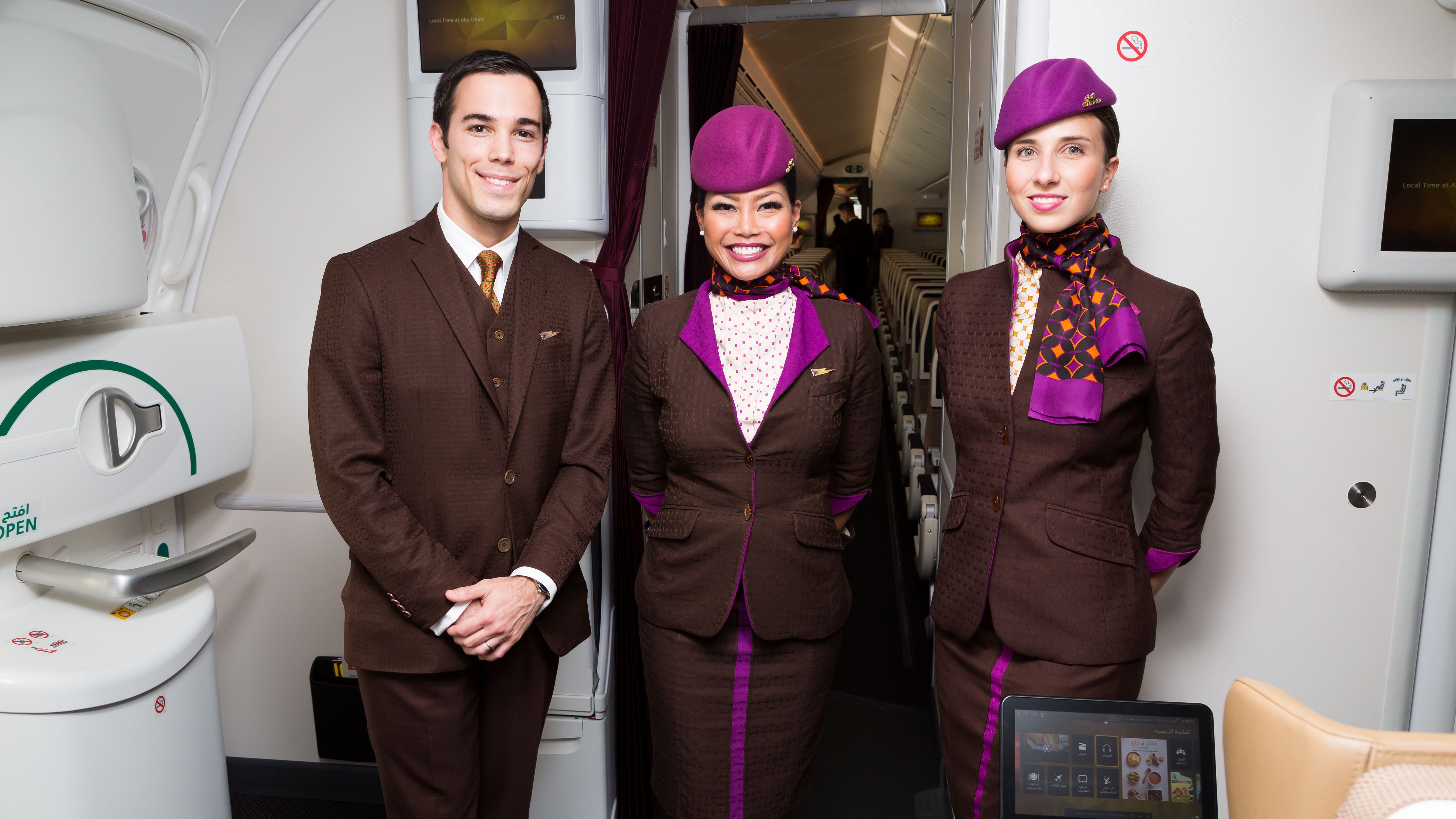 Three Etihad cabin crew members standing in a widebody aircraft.