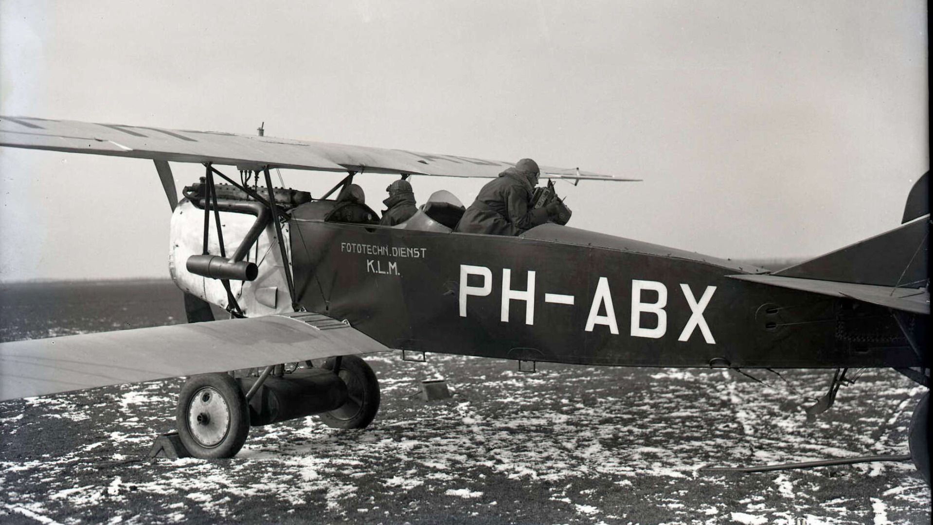 A black and white photo of a KLM Fokker-C.II flying above terrain in 1924.