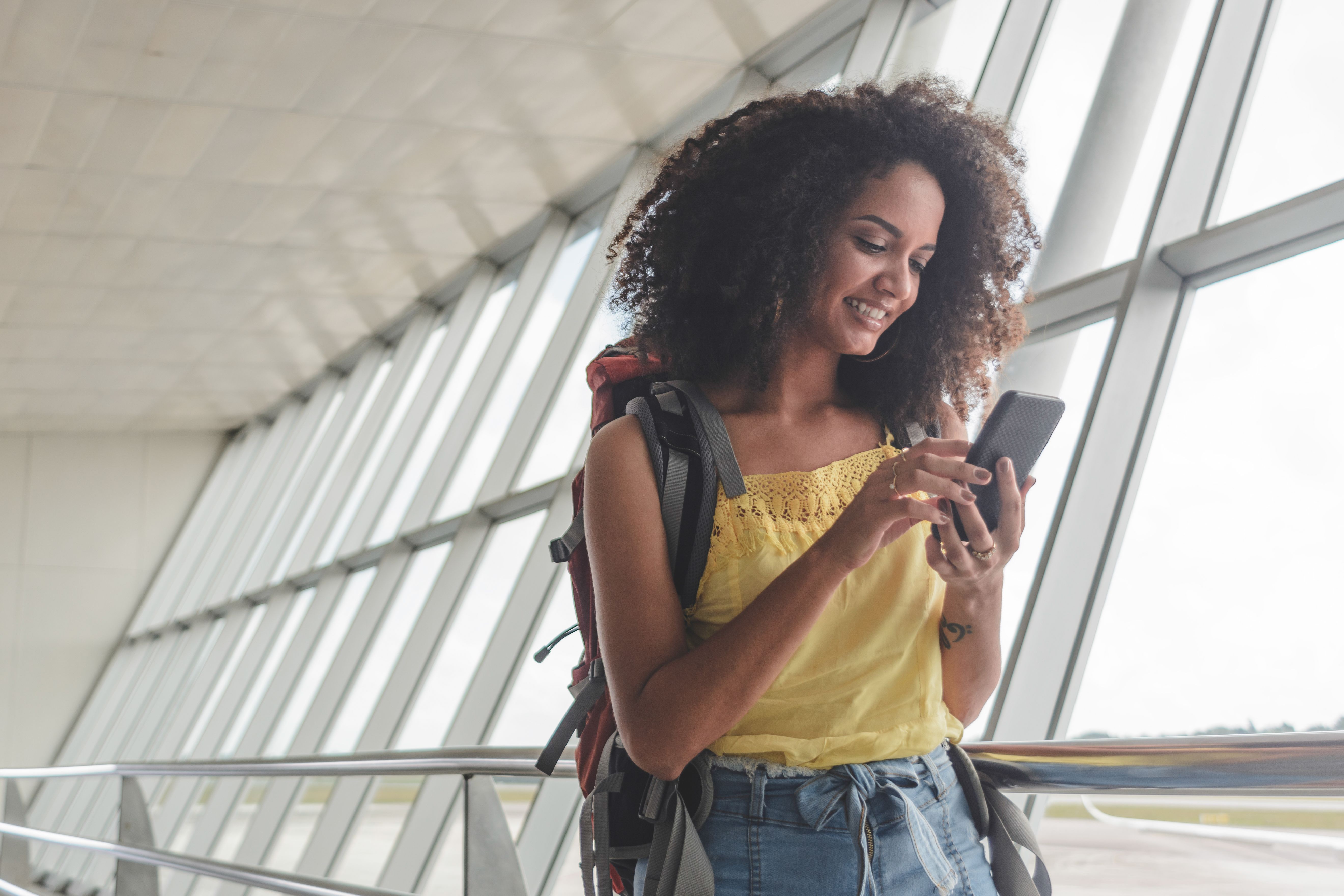 A young woman with a backpack checking her boarding pass on her phone