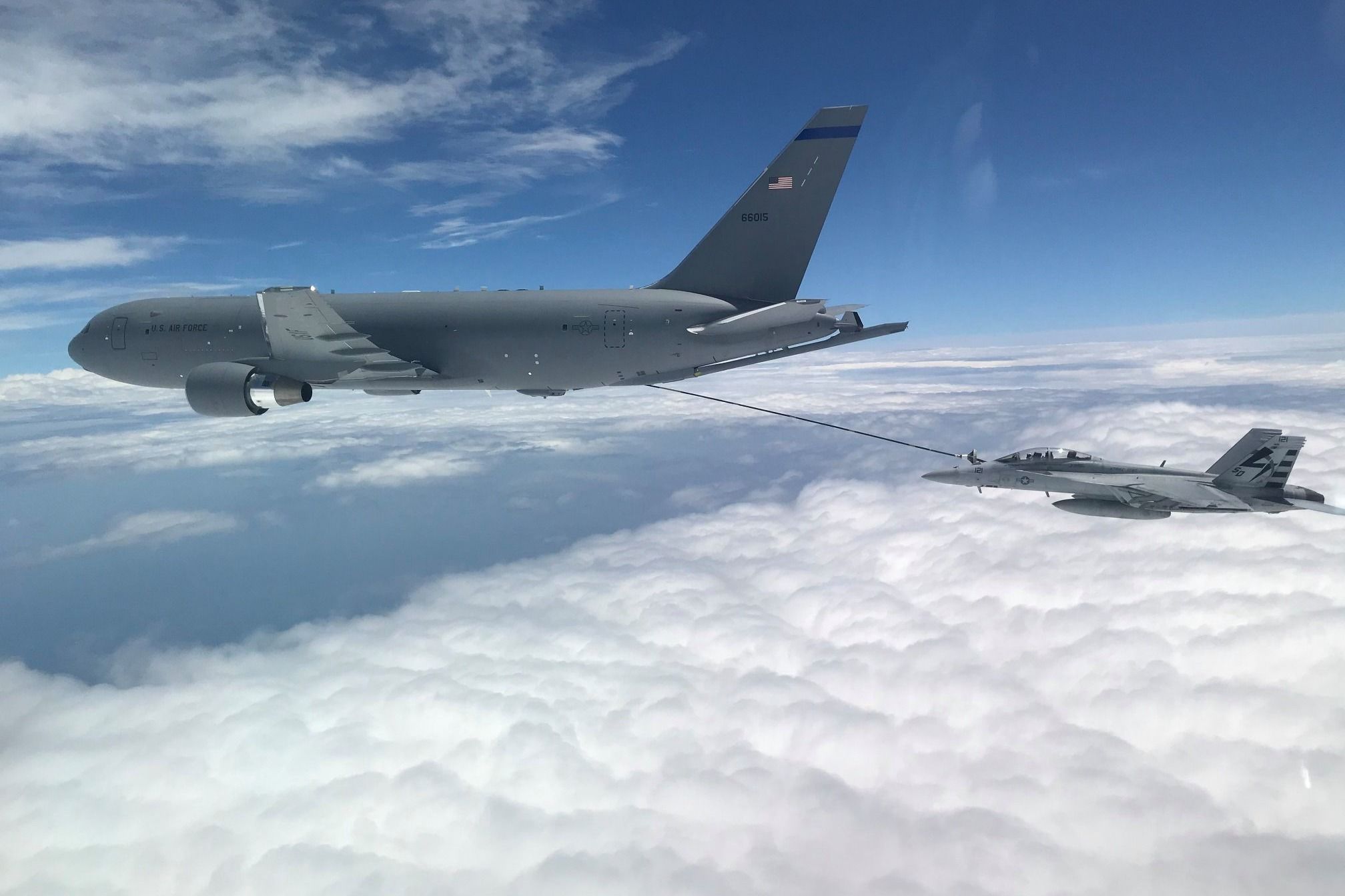 A Boeing KC-46 refueling a fighter jet above the clouds.