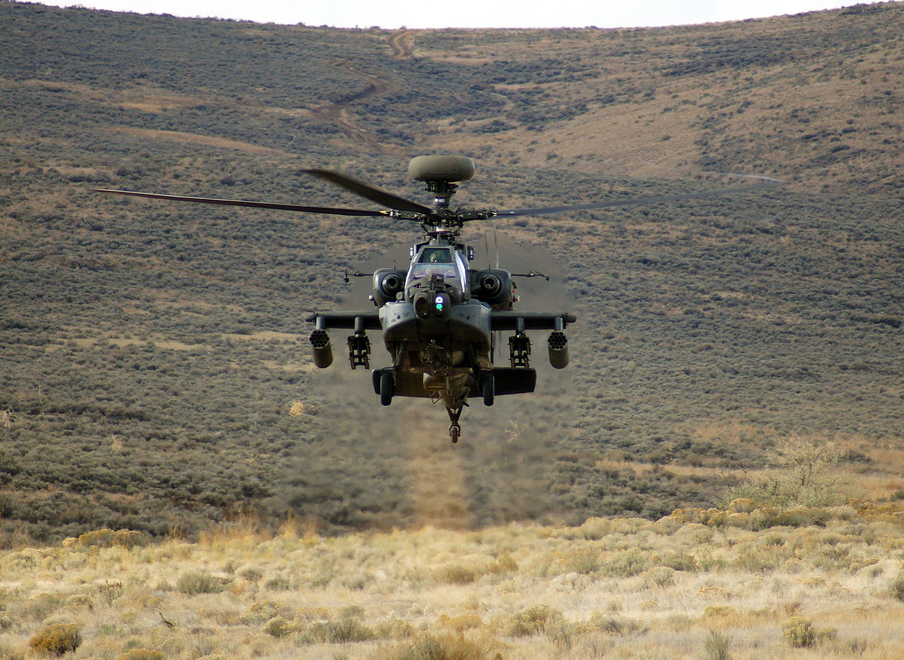 An AH-64 Apache rises from behind a hill.