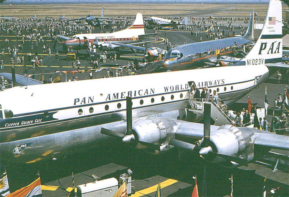 A PAA Boeing 377 Stratocruiser parked near several other aircraft, with a crowd of people surrounding it.