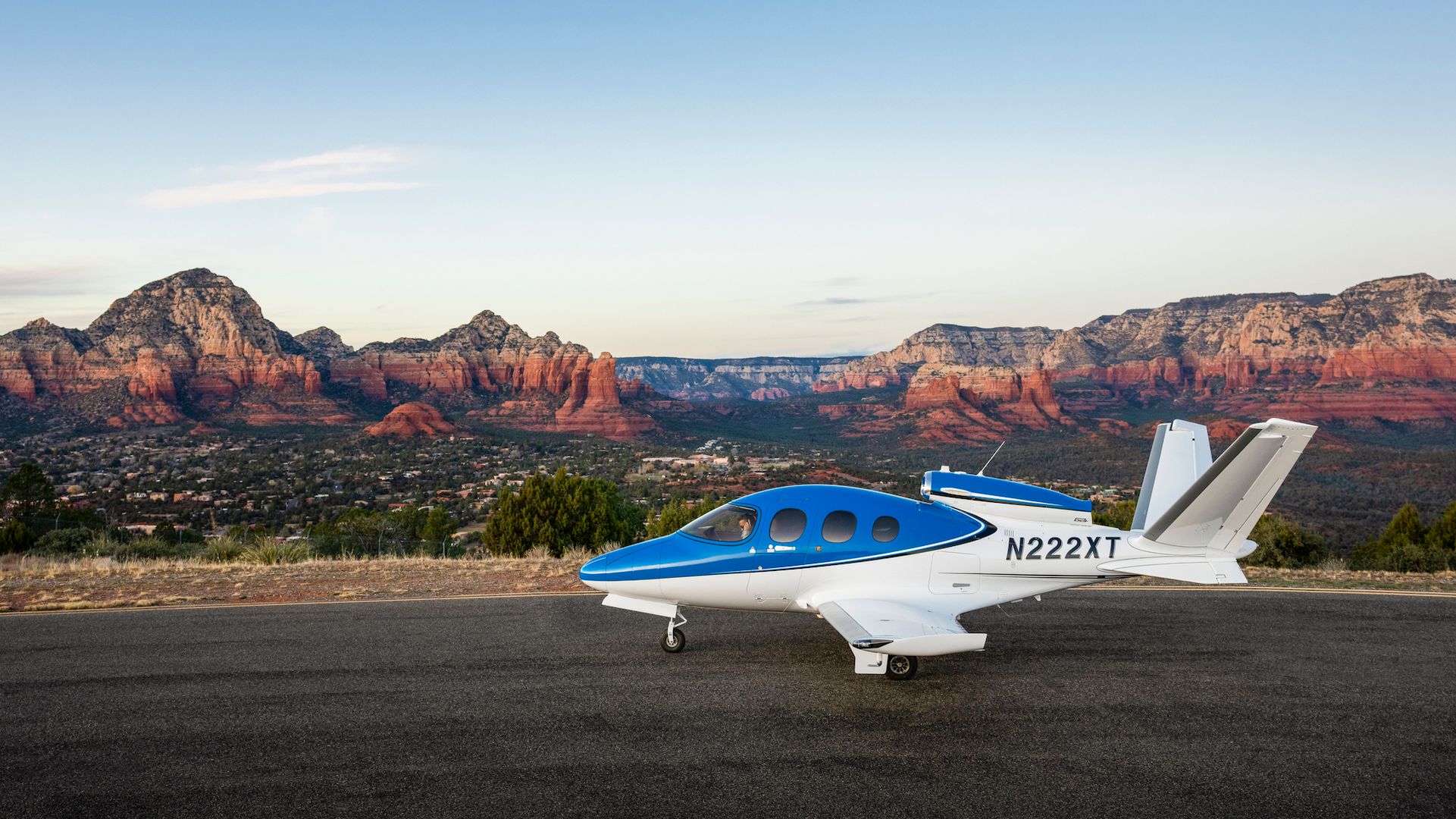 A Cirrus SF50 Vision Jet on an airport apron with mountains in the background.