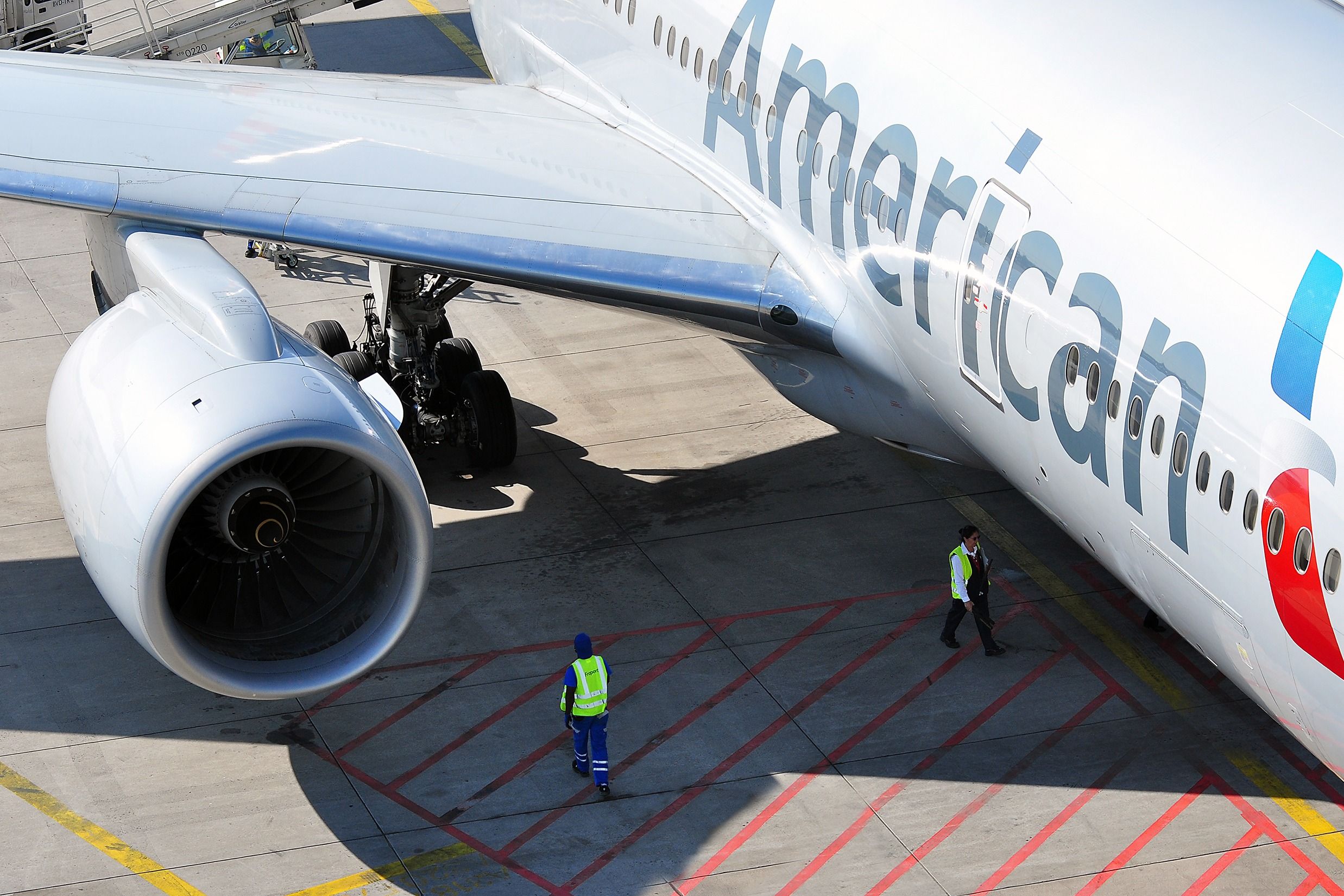 Two workers walking underneath an American Airlines aircraft parked at an airport gate.